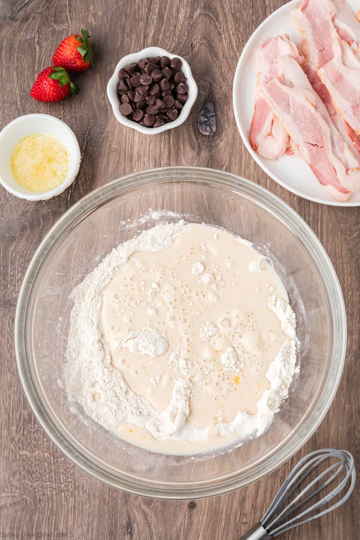 Combining dry ingredients and wet ingredients in a bowl with small bowl of melted butter and chocolate chips on the side