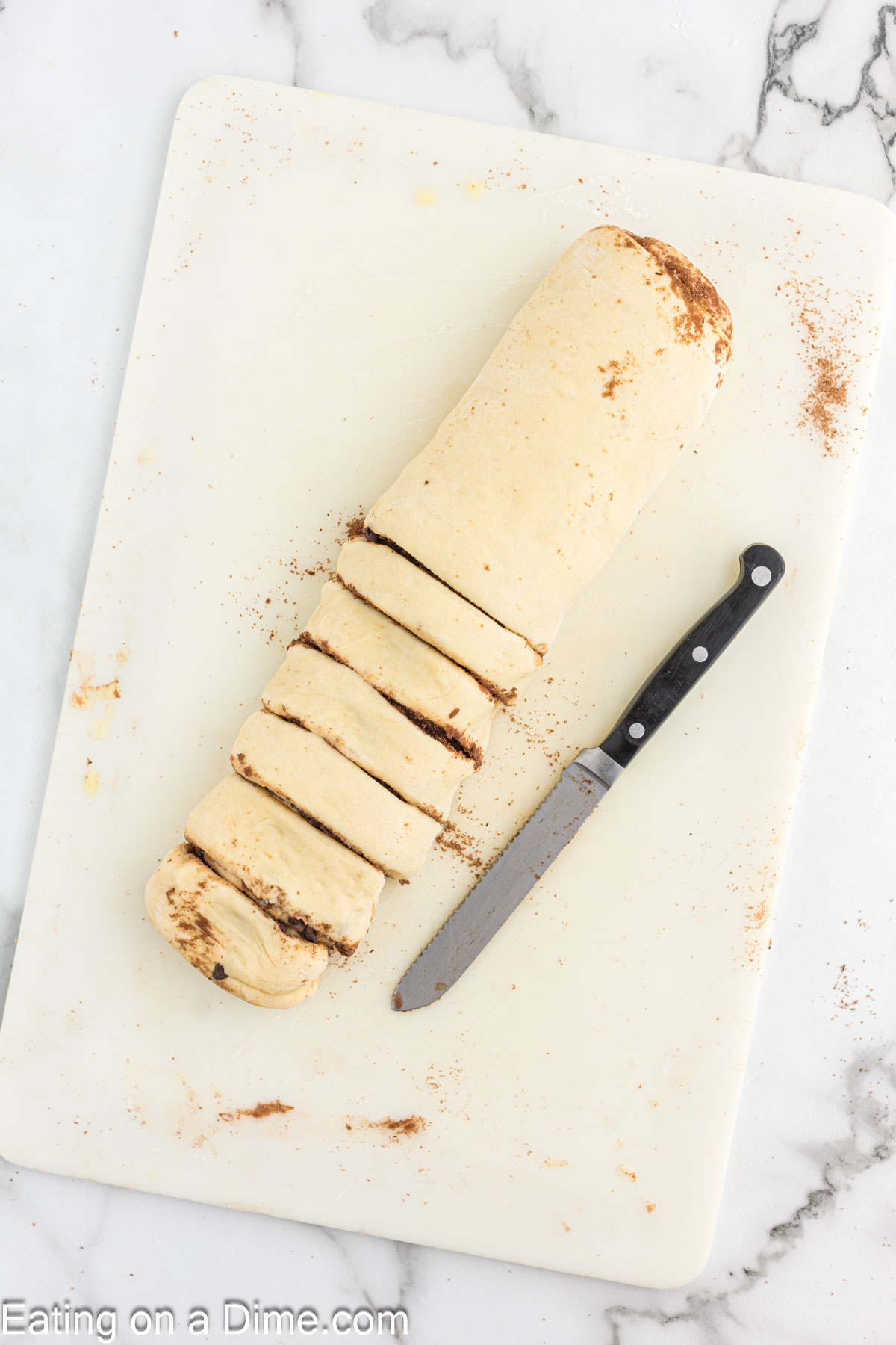 Tube shaped dough on a cutting board with a knife and the dough cut into slits