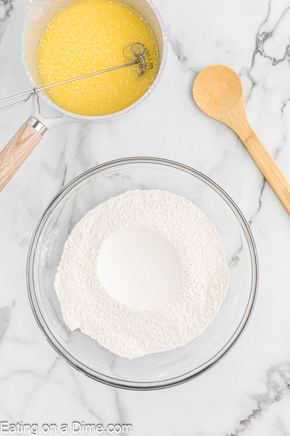 Flour mixture in a bowl with a sauce pan of melted butter on the side with a wooden spoon