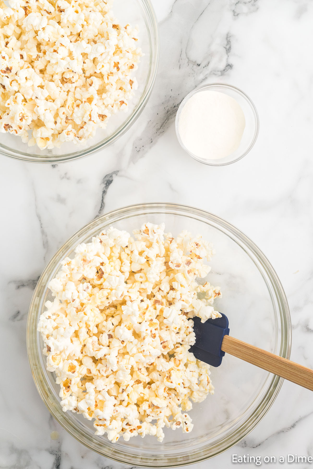 Placing popcorn in a bowl with a bowl of popcorn on the side of seasoning in a bowl