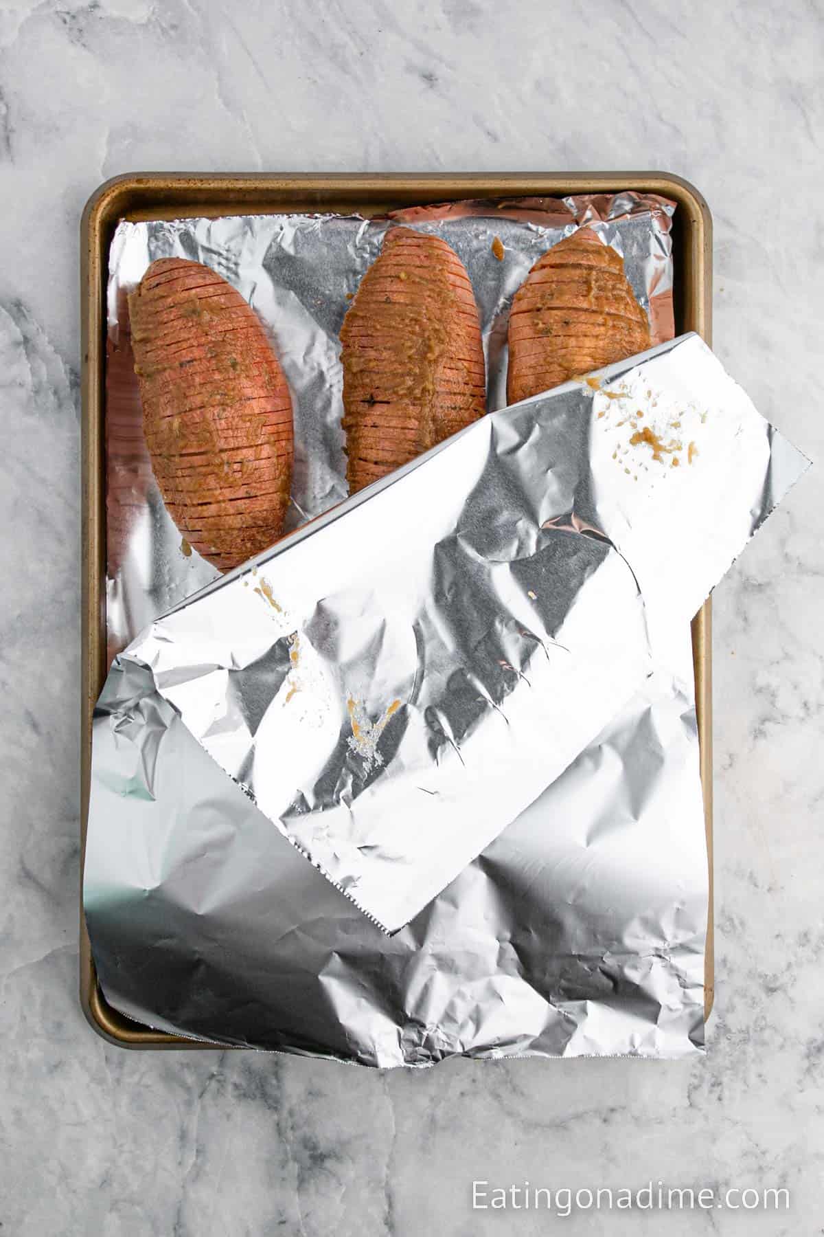 Foil covering the sweet potatoes on a baking sheet