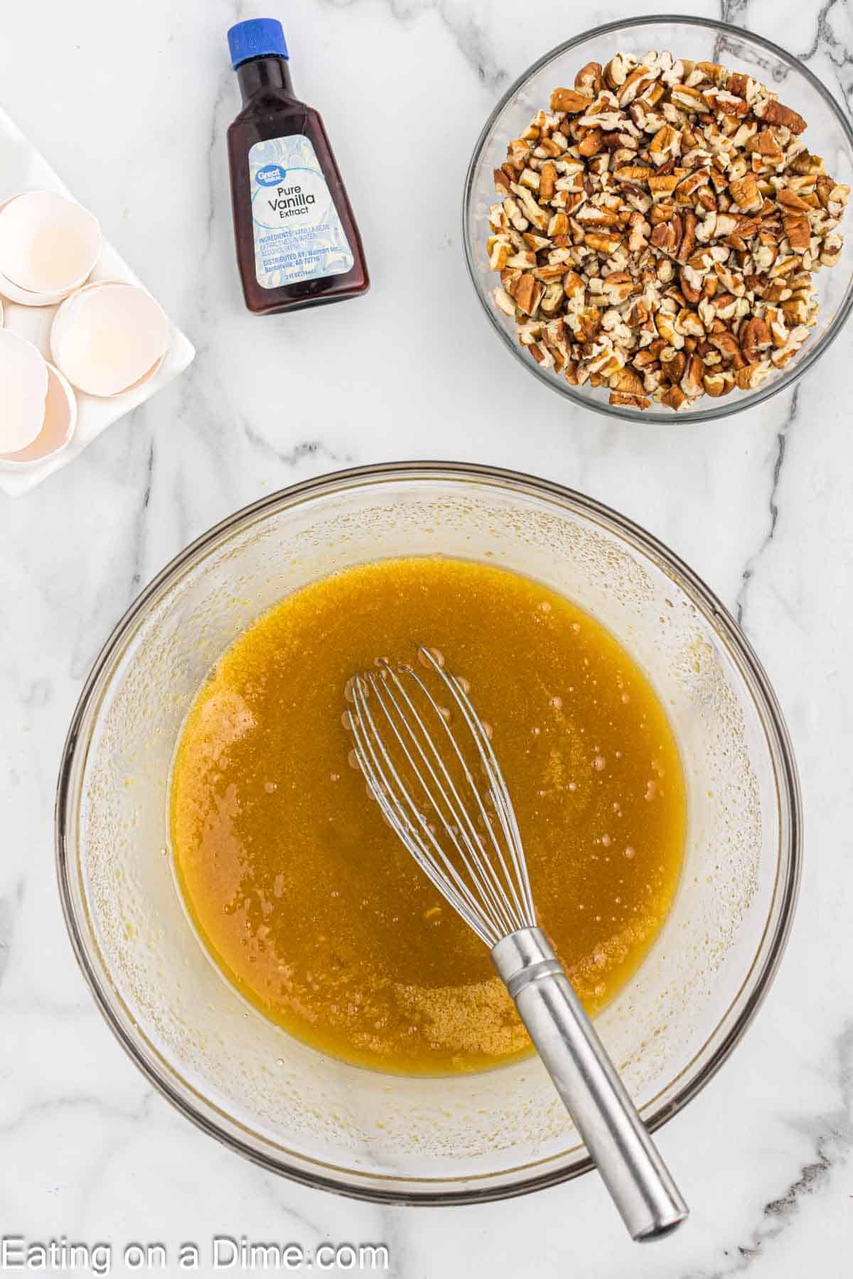 Whisking together pecan pie filling in a bowl with a small bowl of chopped pecans on the side