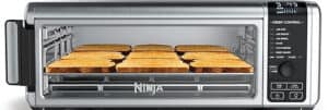 A sleek stainless steel toaster oven, featuring the versatility akin to the best stainless steel air fryers, showcases multiple buttons and settings. Inside, nine slices of evenly toasted bread rest perfectly on a wire rack, beneath an illuminated digital display.