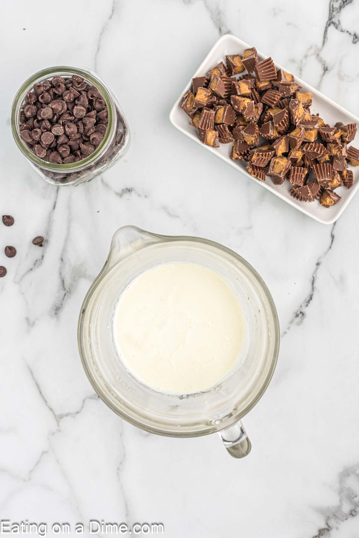 Heavy Cream in a large glass measuring cup with a side of chocolate chips and a plate of Reese's Peanut Cups