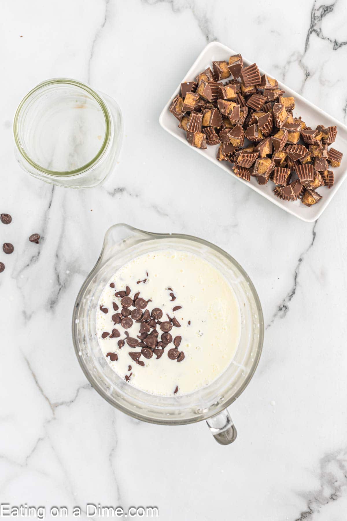 Heavy Cream with chocolate chips in a large glass measure cup with a plate of Chopped Reese's Peanut Cups