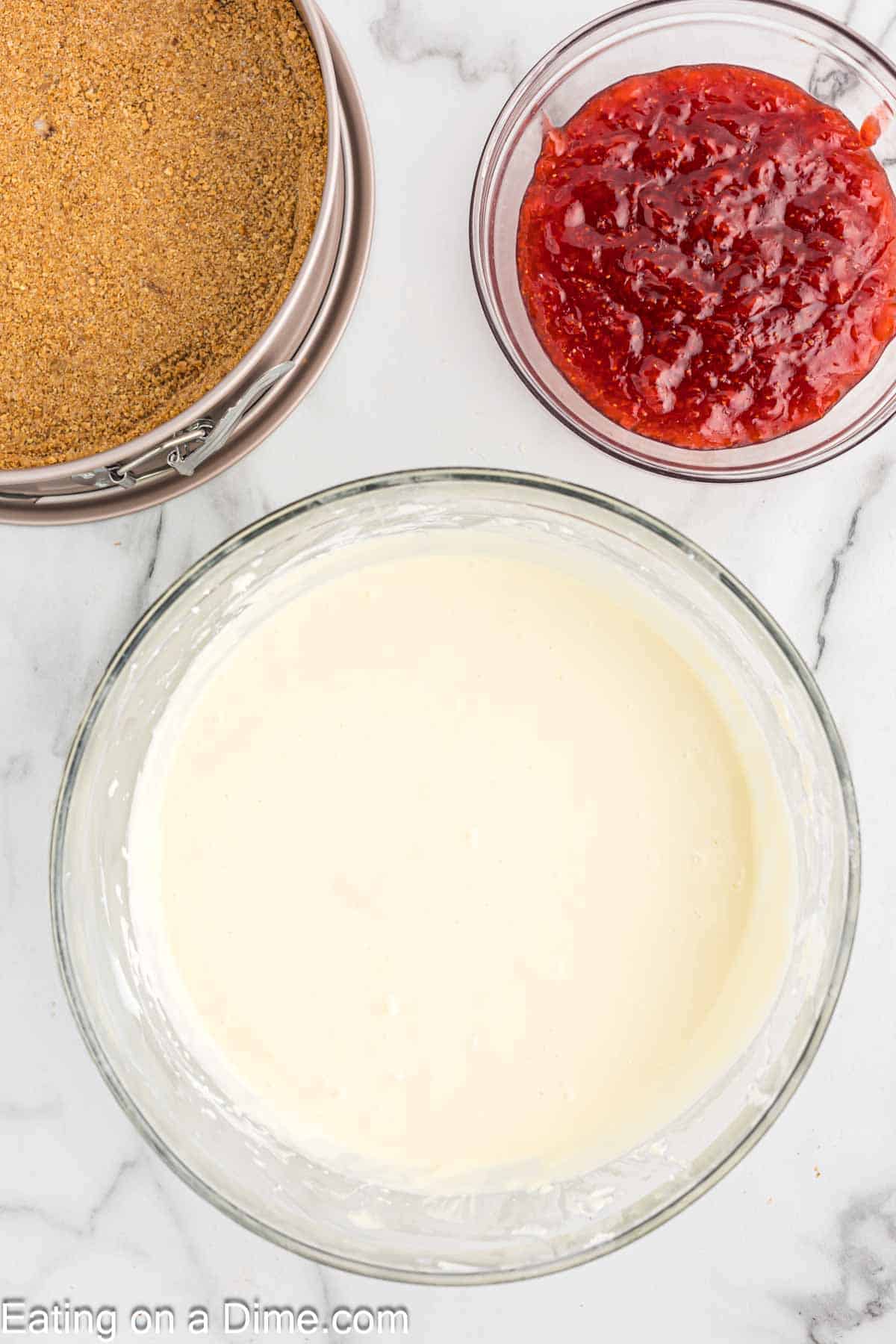 Sour cream and heavy cream mixed with the cream cheese mixture with graham cracker crust pan and a bowl of strawberry swirl