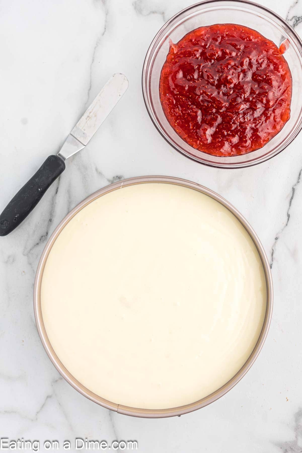 Cheesecake mixture in the springform pan with a bowl of the strawberry sauce