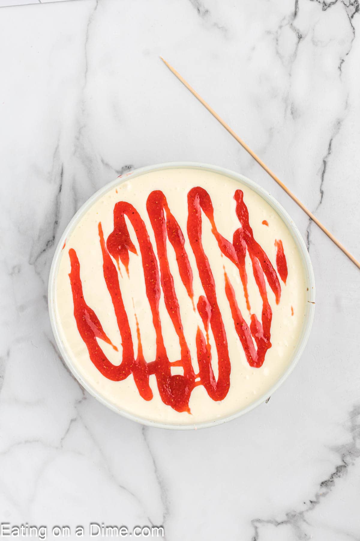 Drizzling the strawberry mixture on top of the cheesecake batter in the pan