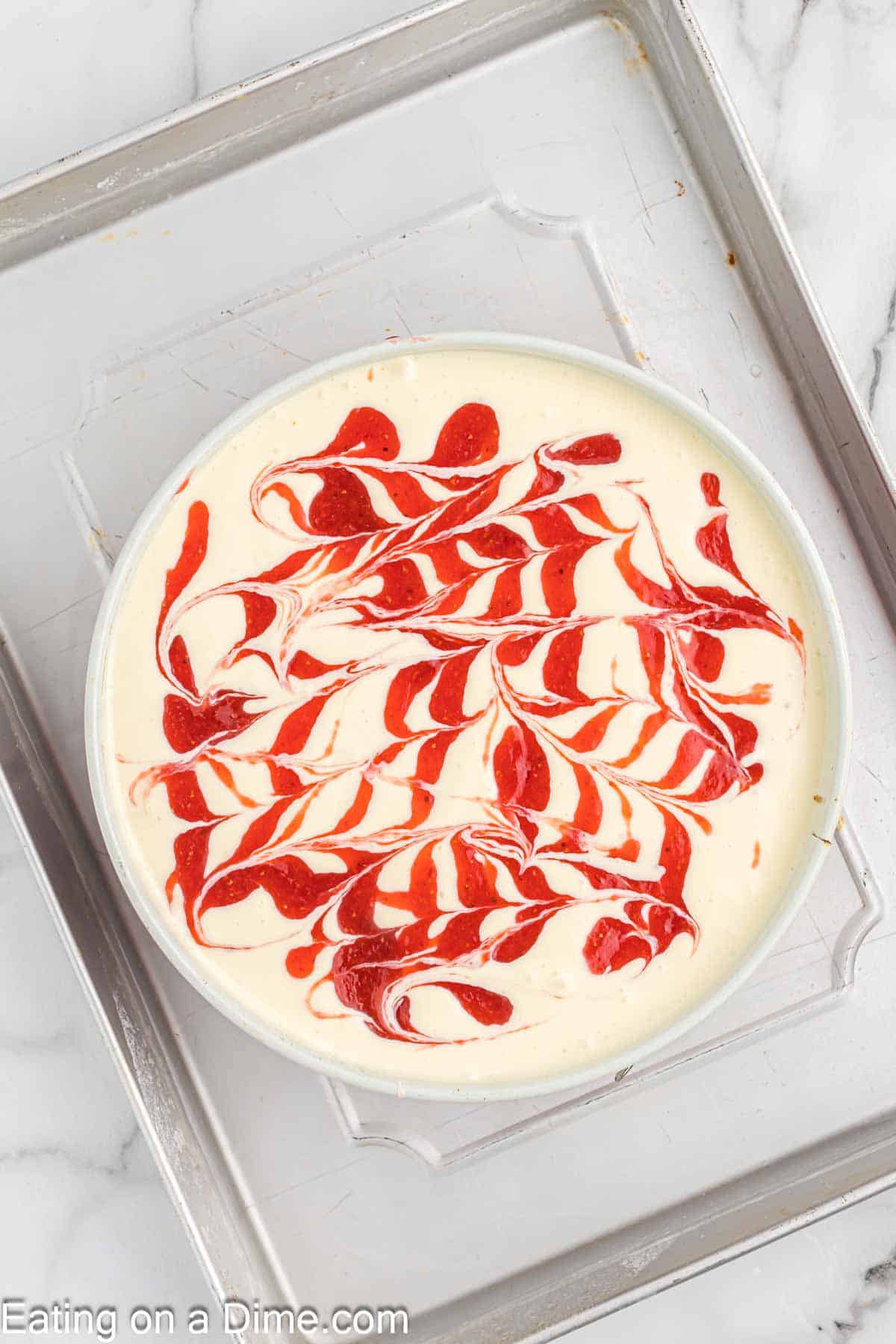 Placing the cheesecake topped with the strawberry swirl on a baking sheet with water