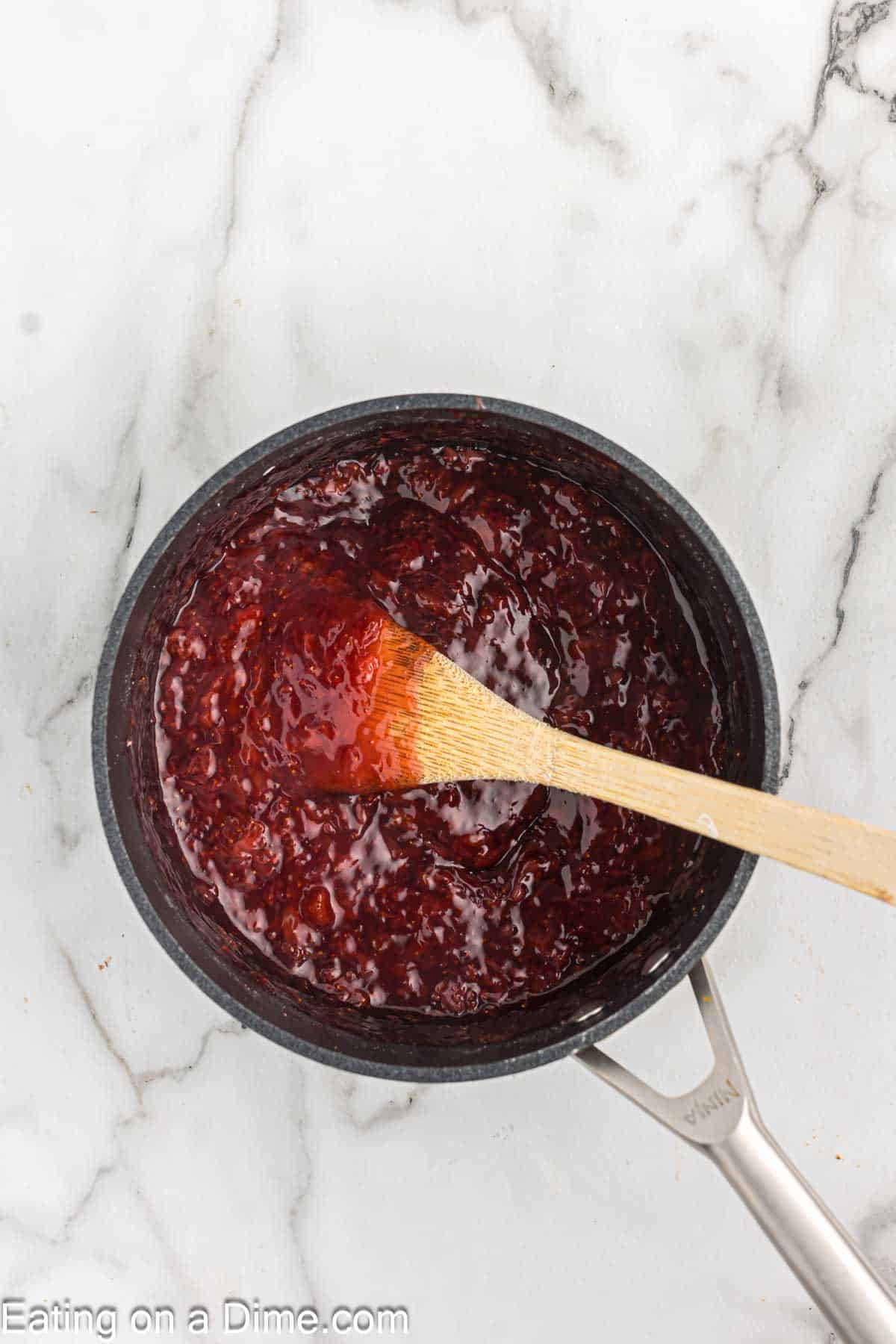 Heating the strawberry mixture in a saucepan with a wooden spoon