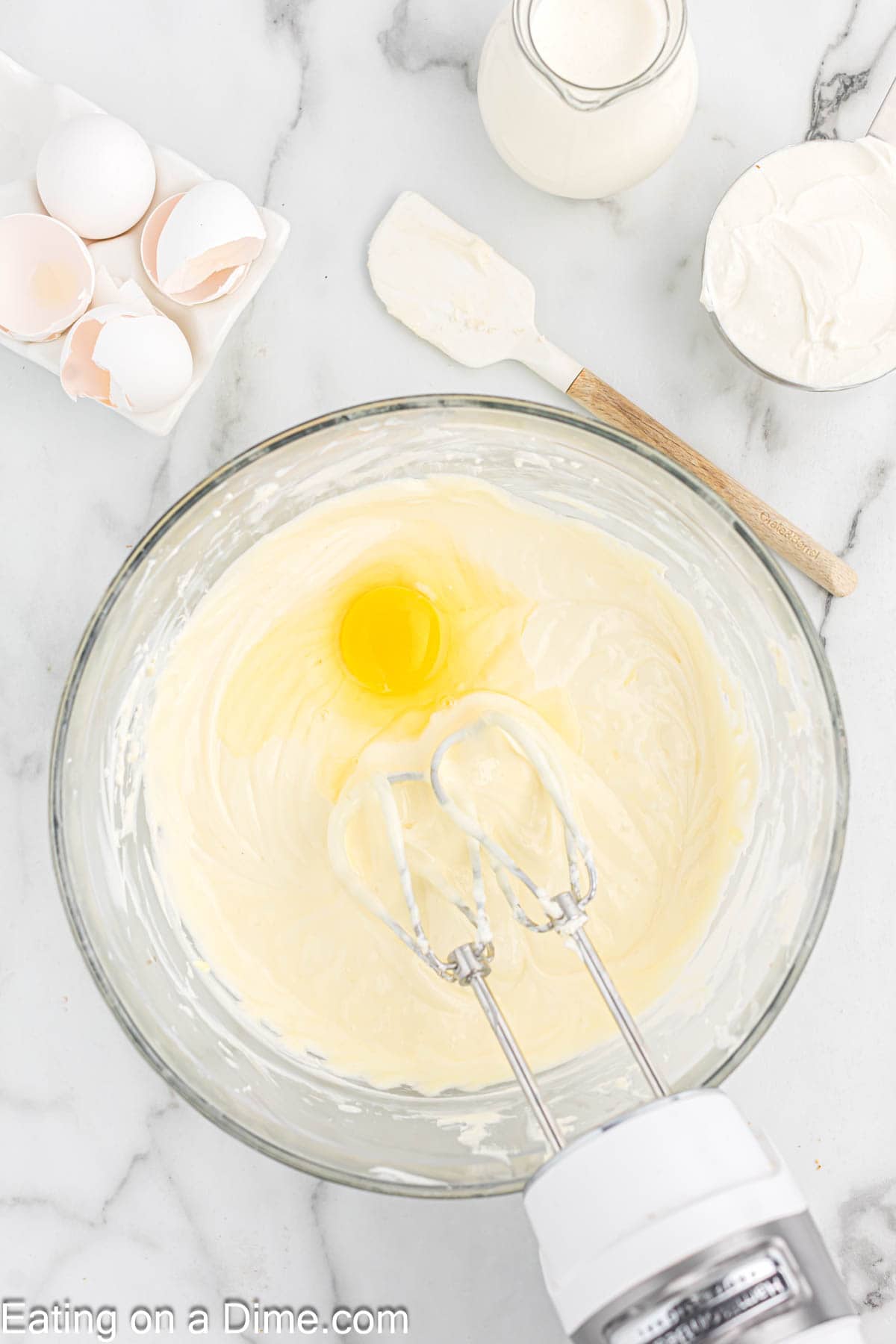 Adding in eggs to the cream cheese mixture in a bowl with a hand mixer