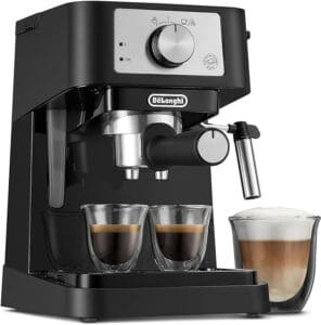 A black DeLonghi espresso machine, one of the best budget espresso machines, features two small espresso cups beneath its dual spout. With a milk frother attached on the side, it creates a perfect cup of frothy coffee that sits enticingly nearby.