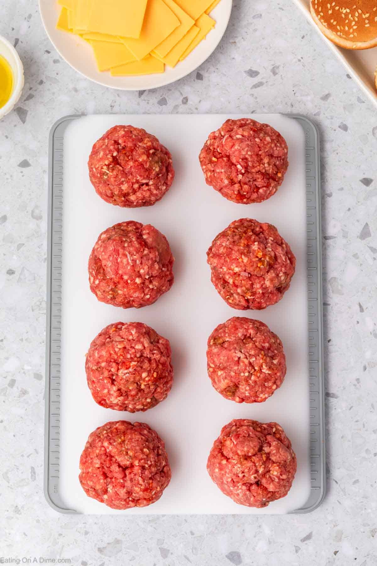 Ground beef balls on a cutting board with a plate of slice cheese on the side