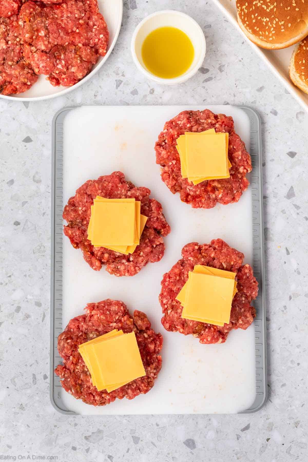 Ground beef patties on a cutting board topped with slice cheese