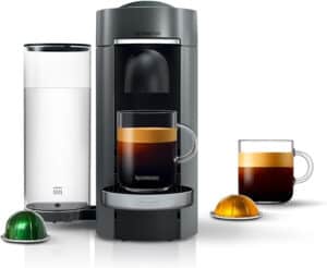 A sleek Nespresso, one of the best budget espresso machines, features a transparent water tank brewing a rich cup of espresso. Beside it, a full glass of coffee and two capsules—one green and one gold—highlight versatile brewing options.