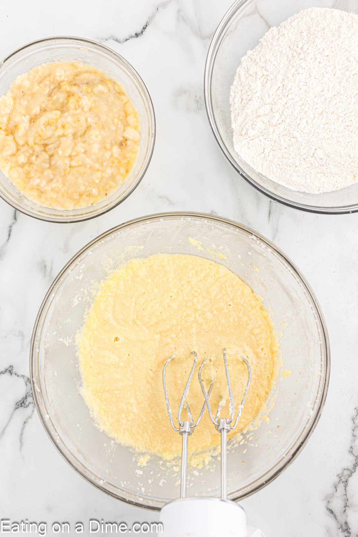 Combining the butter mixture with eggs with a bowl of mashed bananas and flour on the side