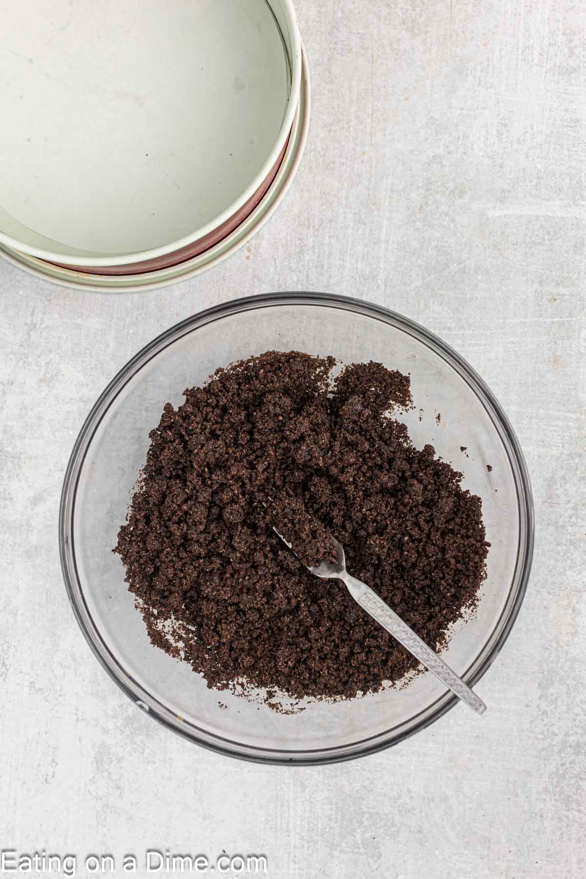 Crushed Oreo Cookies in a bowl with melted butter with a pie crust on the side