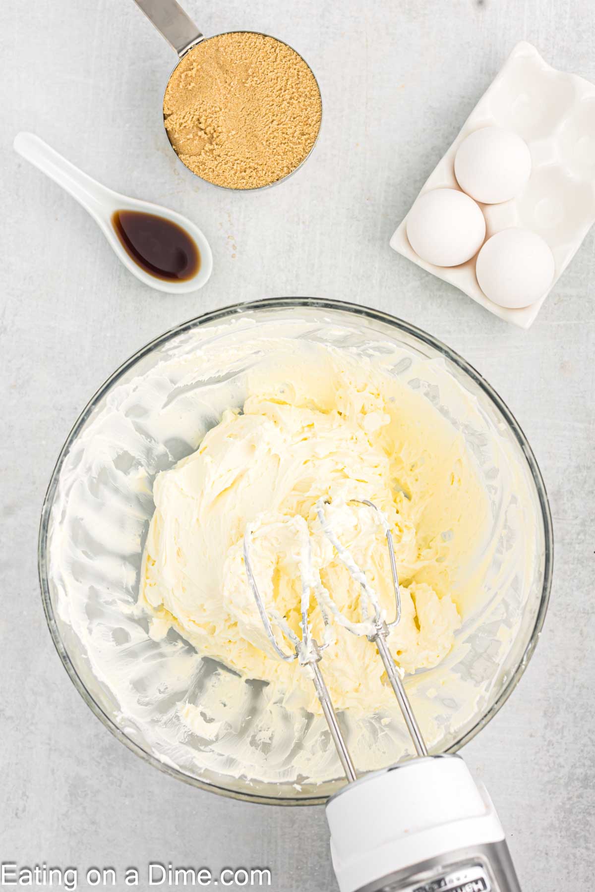 Beating cream cheese with a hand mixer, with a side of brown sugar, vanilla extract and eggs