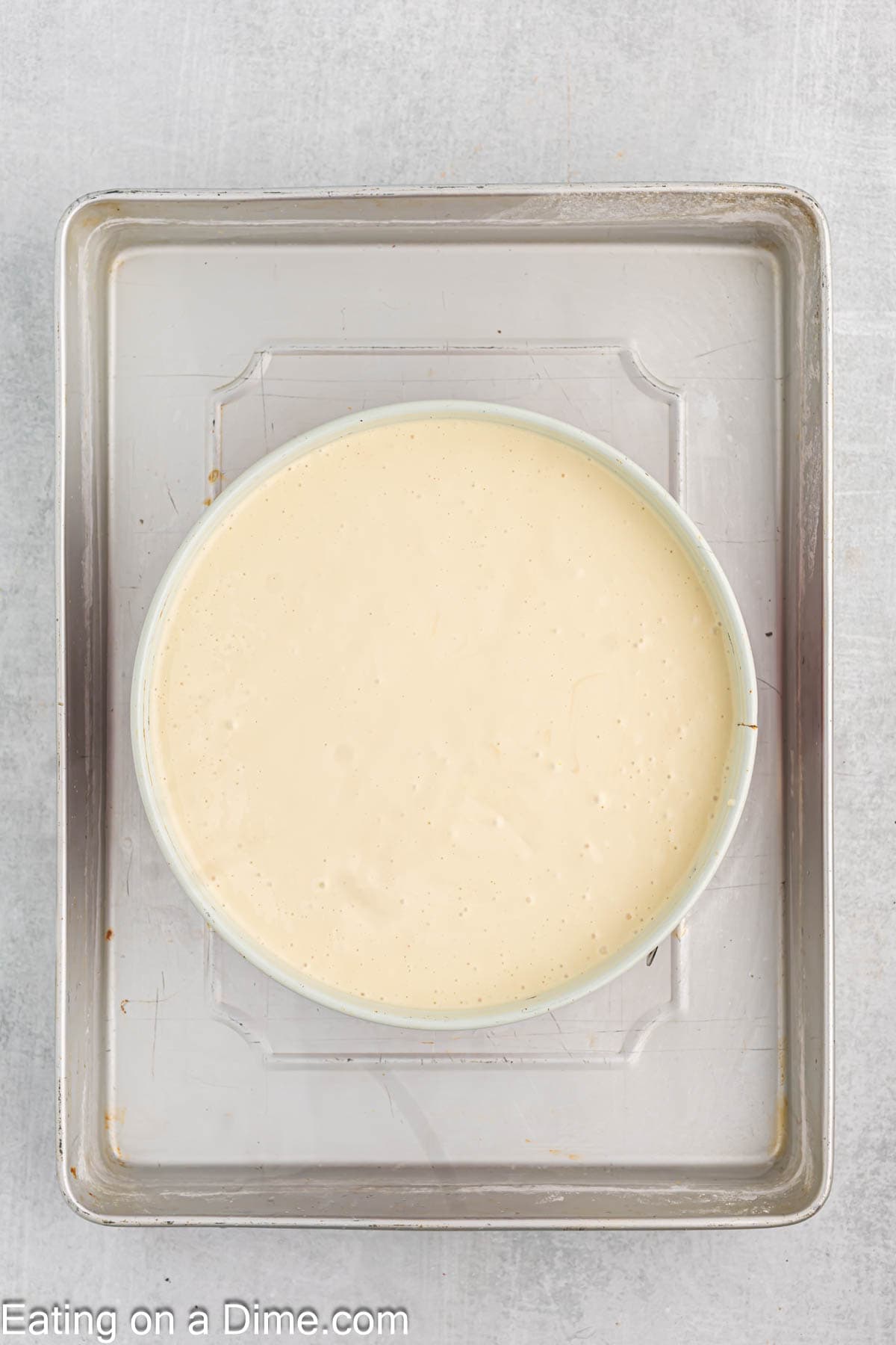 Pouring the cheesecake batter into the pie plate on a baking sheet