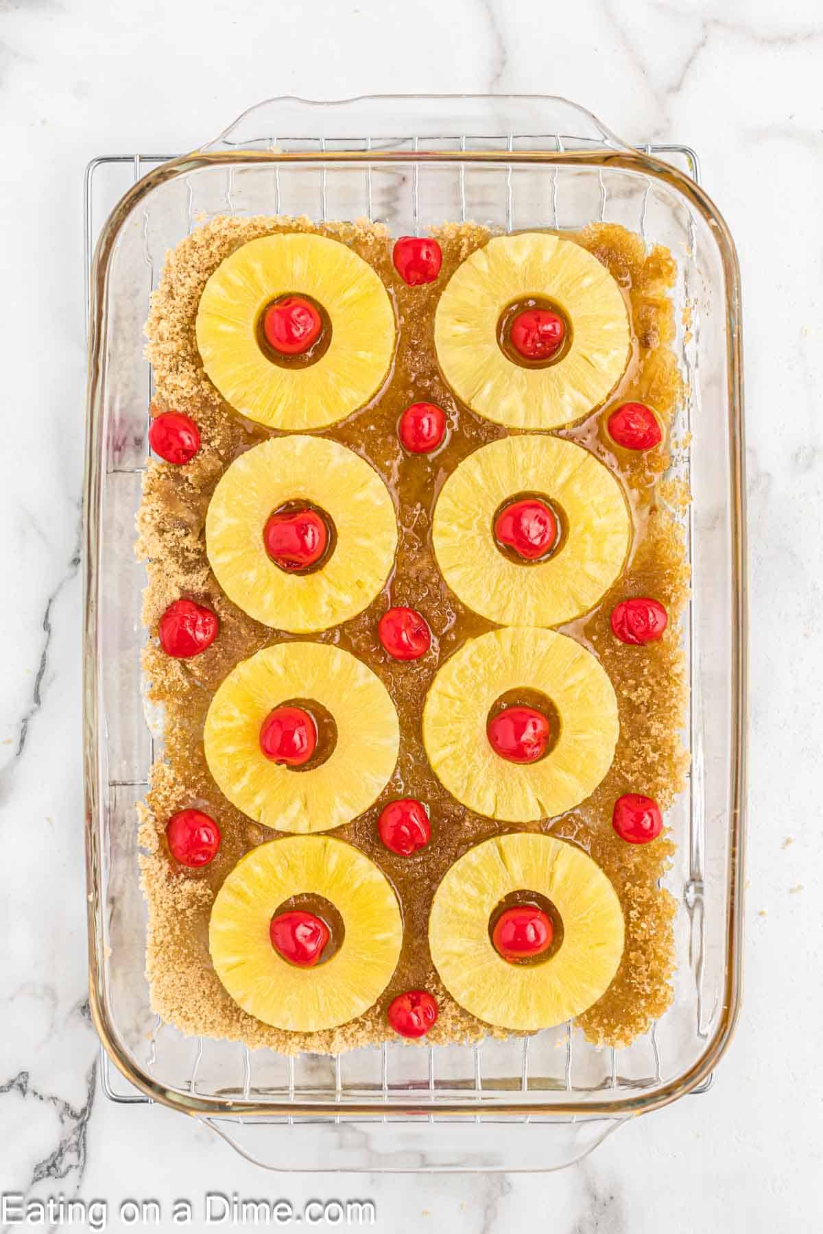 Topping the brown sugar mixture with slice pineapple rings and cherries