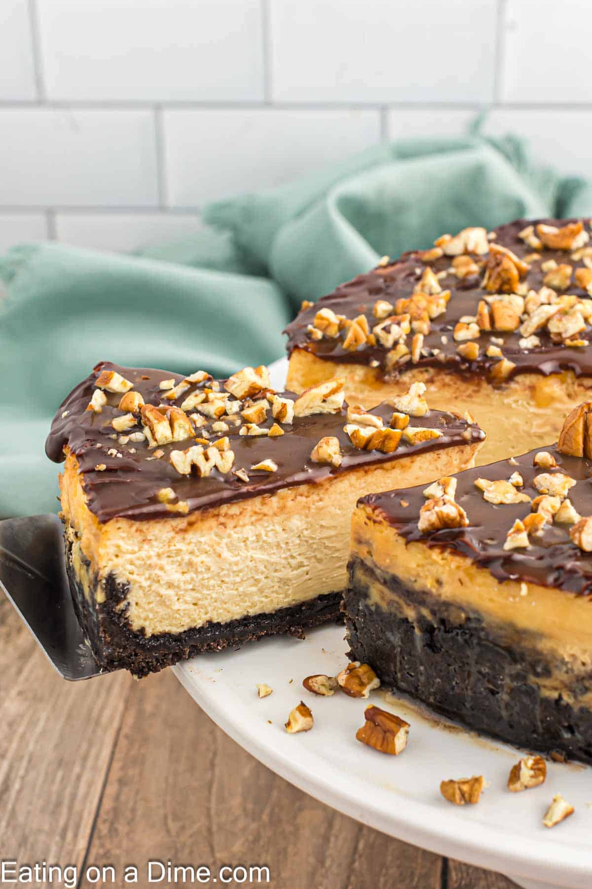 Turtle Cheesecake on a cake stand with a slice cut on a spatula