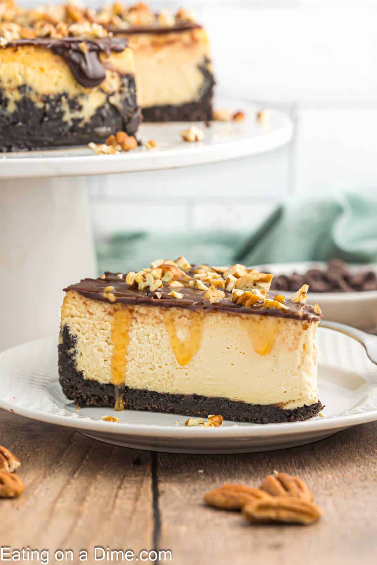 Slice of Turtle Cheesecake on a plate with Turtle Cheesecake on a cake stand