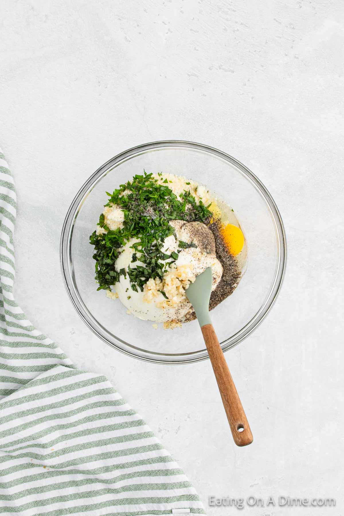 Combining the ricotta cheese, parmesan cheese, egg, garlic, parsley, basil leaves, salt and pepper in a bowl with spatula
