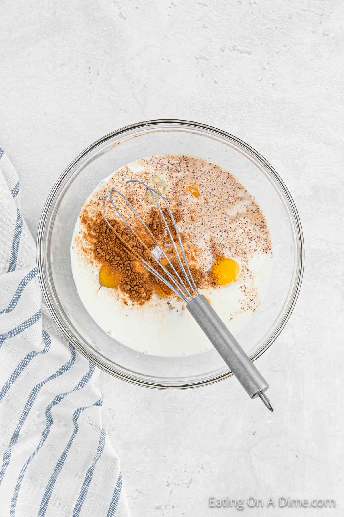 Milk, sugar, vanilla extract, cinnamon and nutmeg in a bowl with a whisk