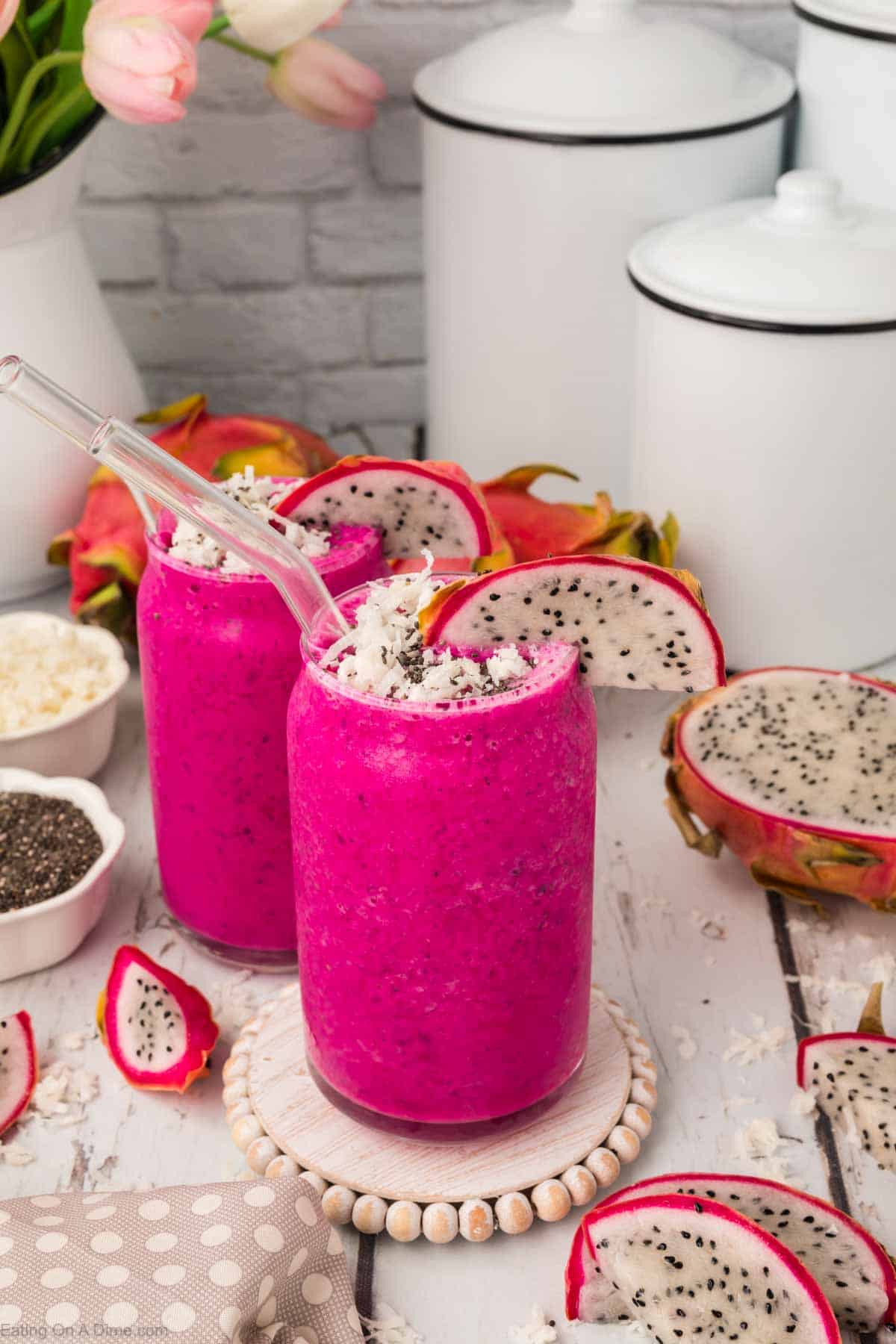 Dragon Fruit Smoothies in a clear glass topped with shredded coconut, slice of dragon fruit with slice of fresh dragon fruit on the sides with bowls of chia seeds and shredded coconut