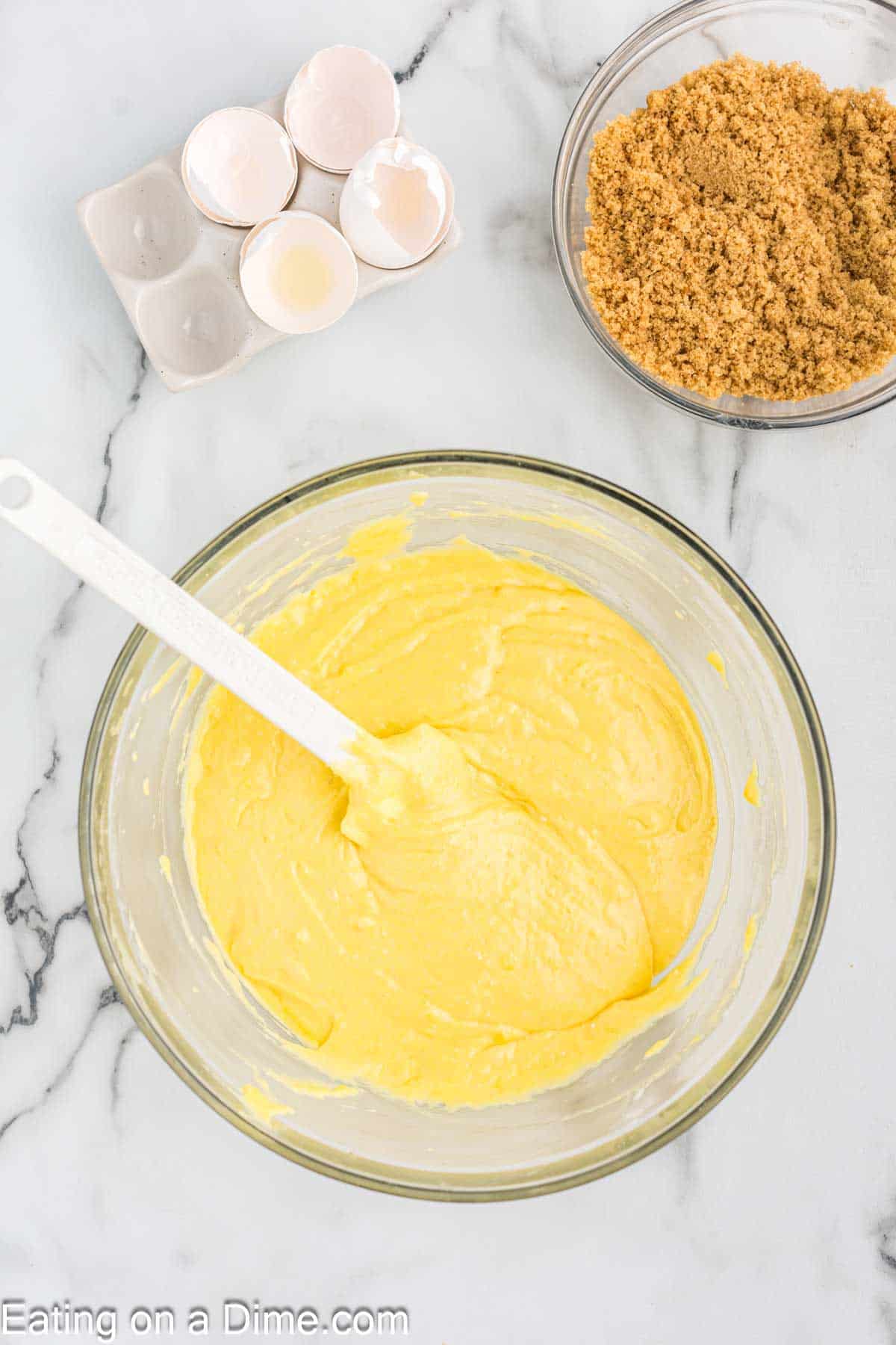 Yellow cake mix, sour cream, eggs, vanilla extract, and oil mixed together in a bowl with a spatula with a bowl of brown sugar on the side