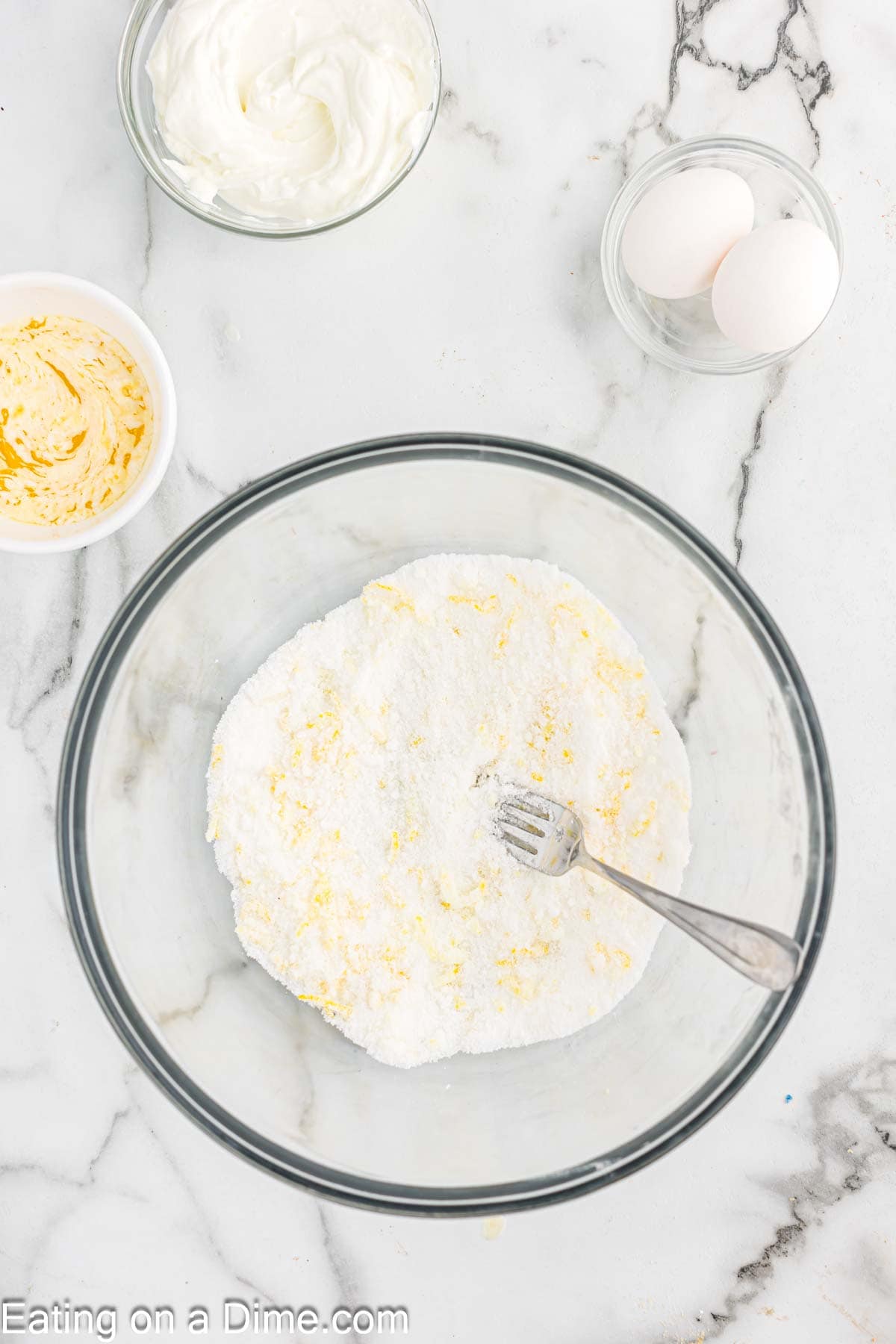 Mixing sugar with lemon zest with a small bowl of melted butter, yogurt and eggs on the side