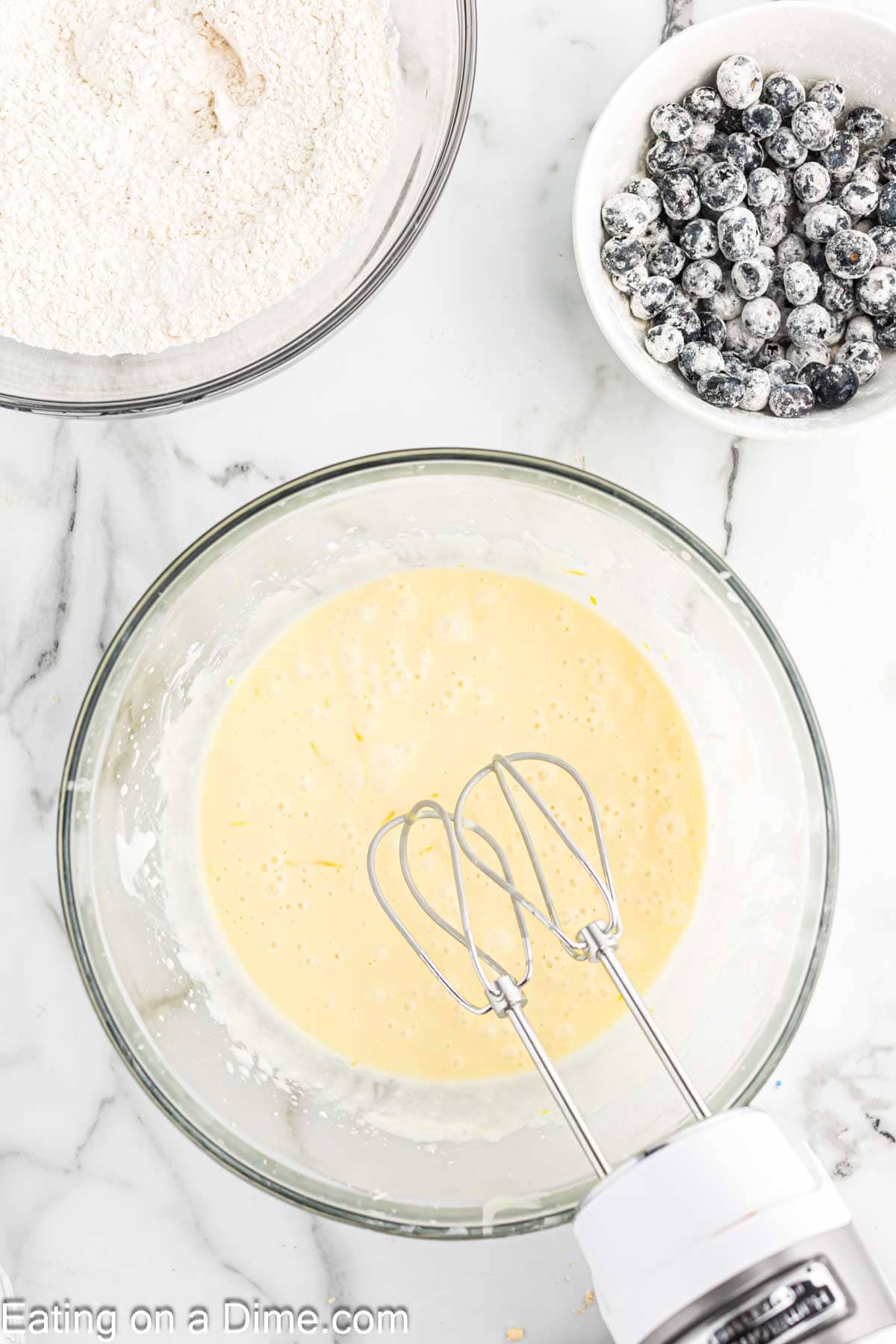 Combining the dry ingredients with the sugar mixture with a small bowl of flour covered blueberries