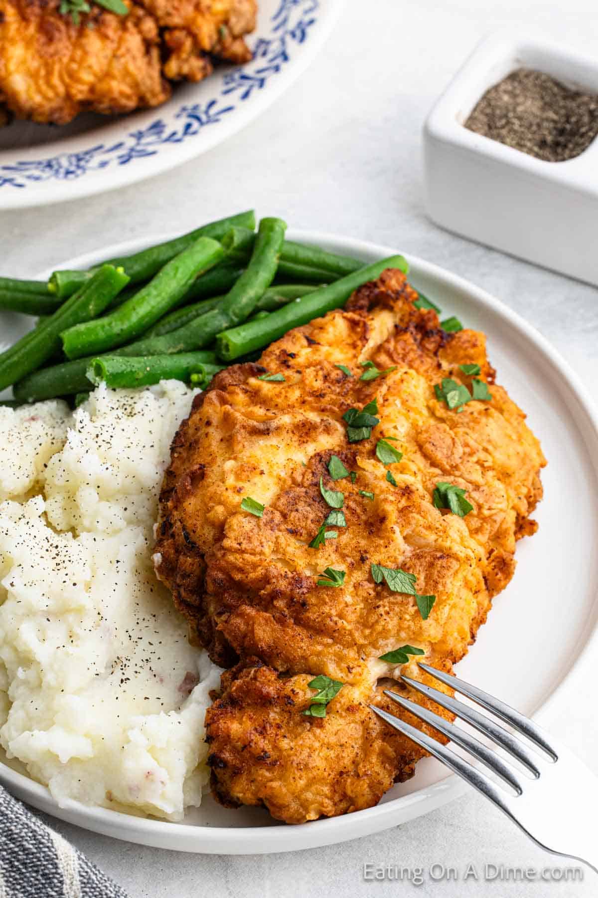 Fried chicken breast on a plate with mashed potatoes and green beans