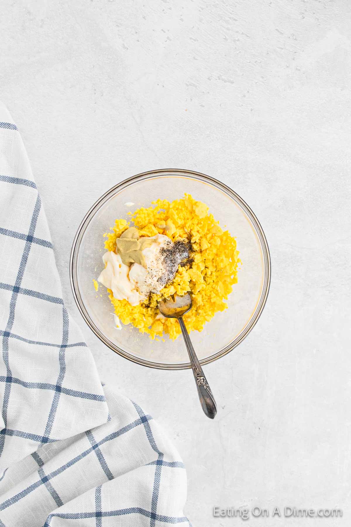 Mashing egg yolks in a bowl with mayo, mustard, and seasoning in a bowl with a fork