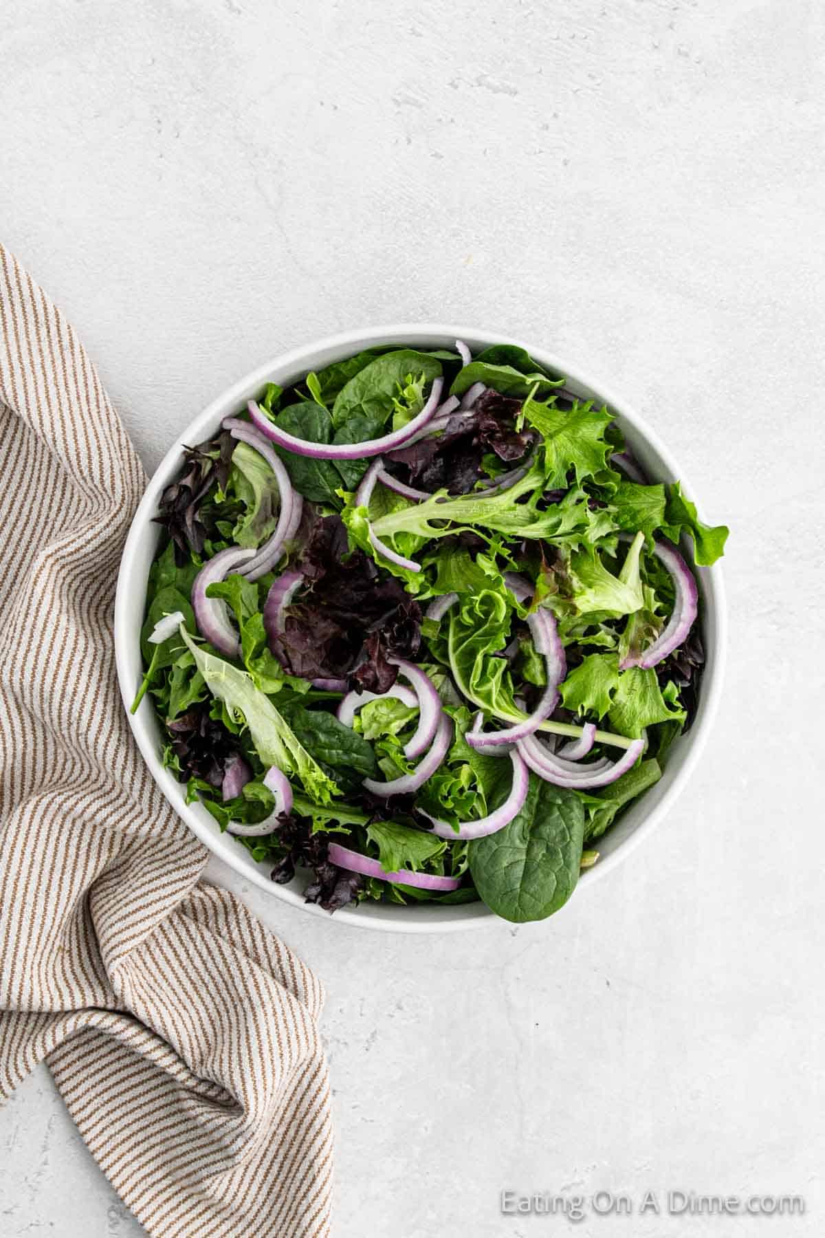 Mixed greens in a bowl topped with red onions
