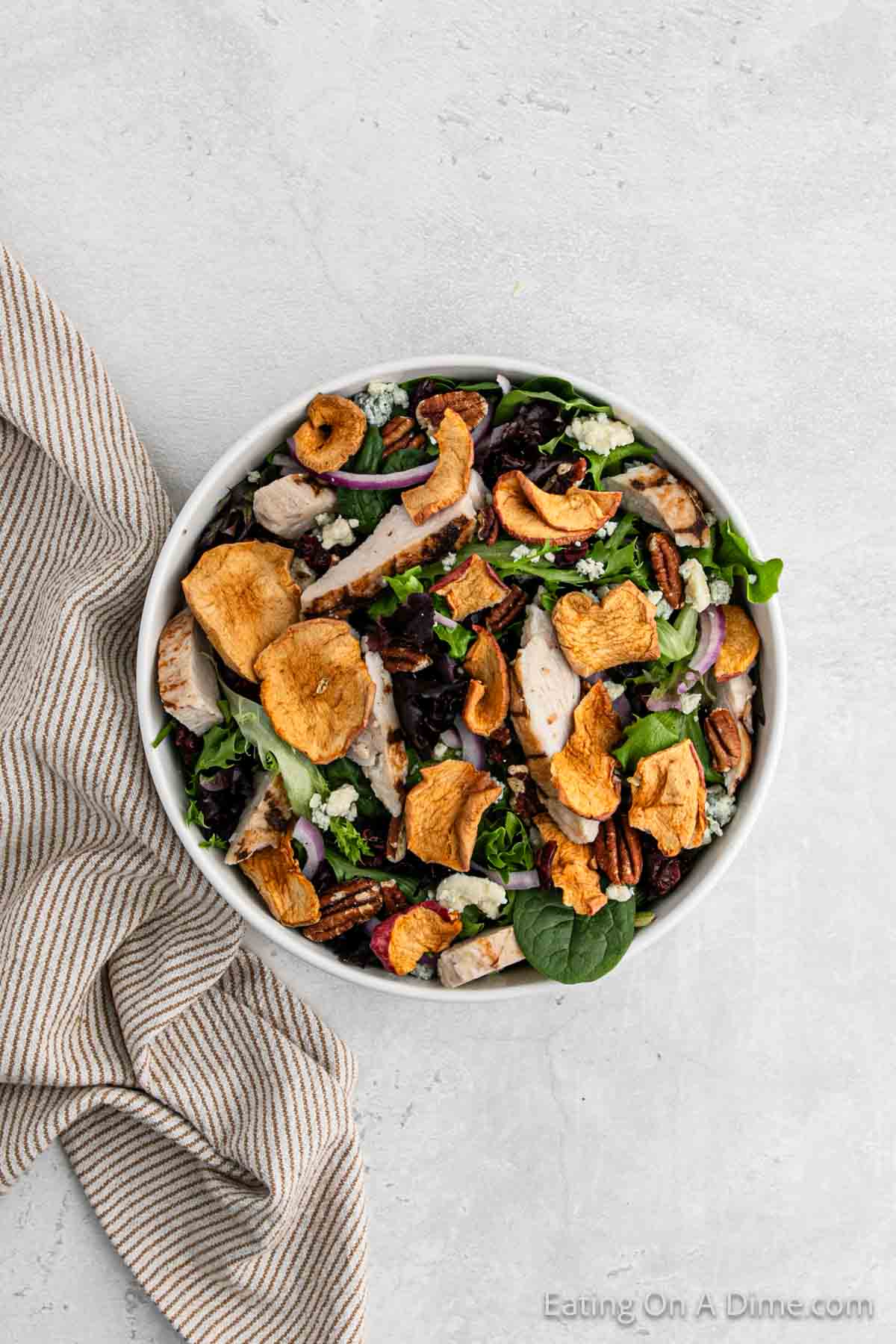 Mixed greens in a bowl topped with red onions, dried apples, grilled chicken