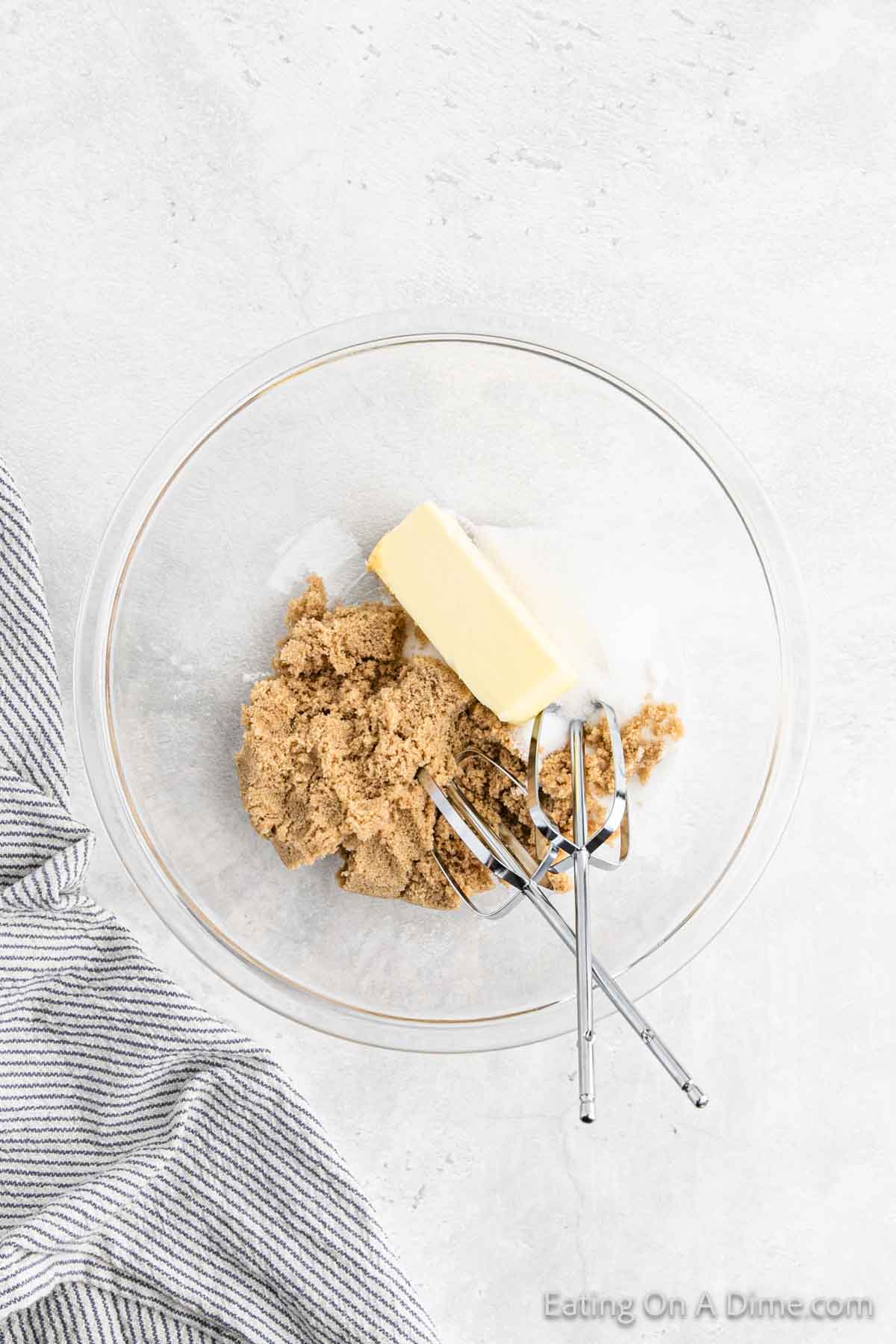 Stick of butter, brown sugar and white sugar in a bowl with stand mixer beaters