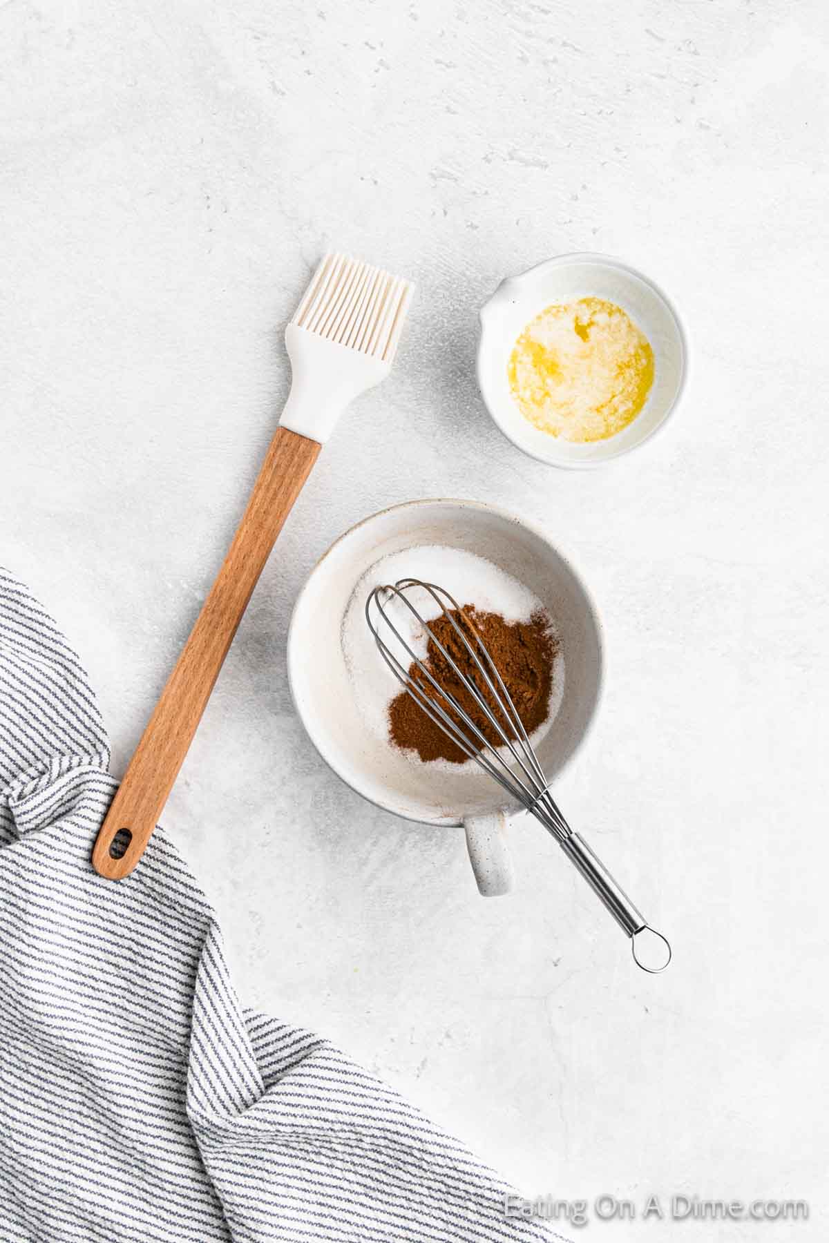 Whisking together cinnamon and sugar in a bowl with a bowl of melted butter and a brush on the side