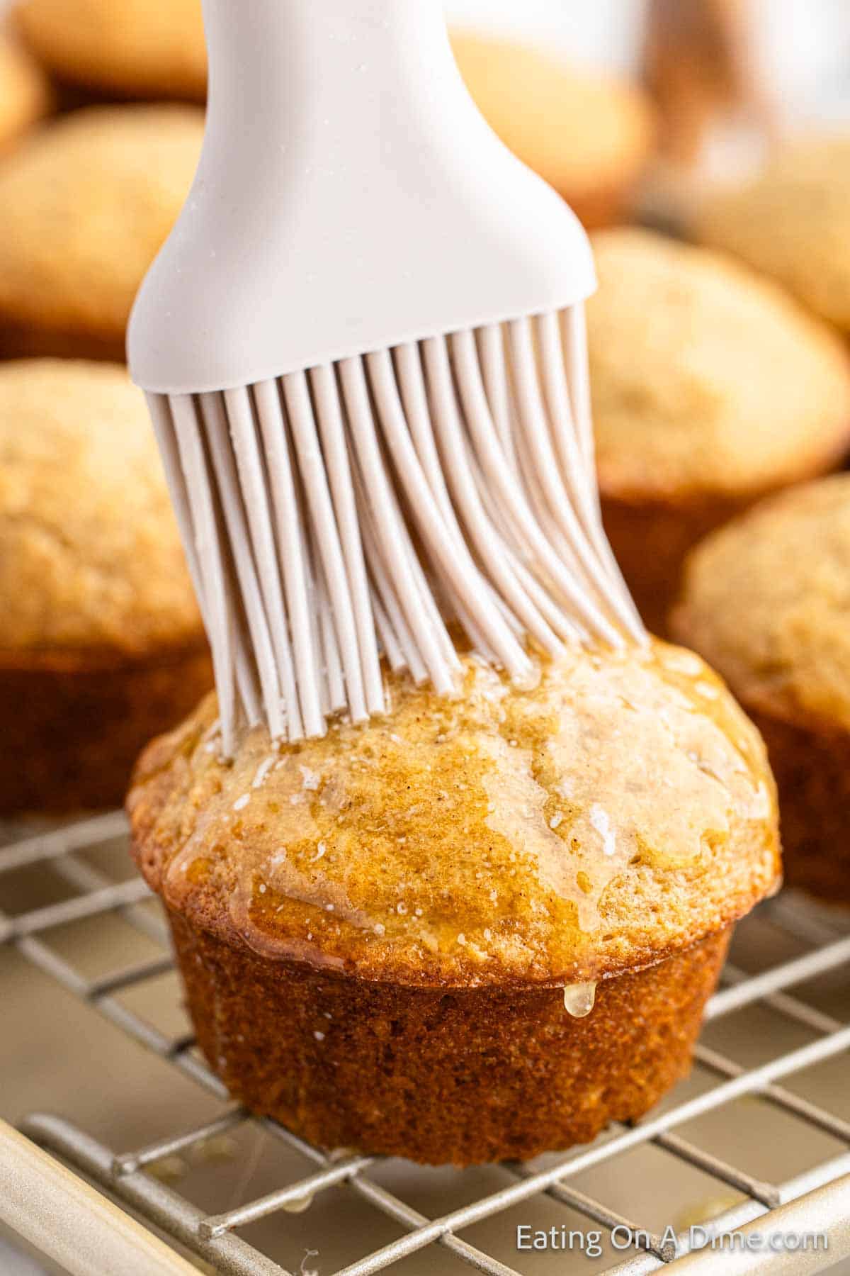 Brushing melted butter over the baked Snickerdoodle muffins on a wire rack