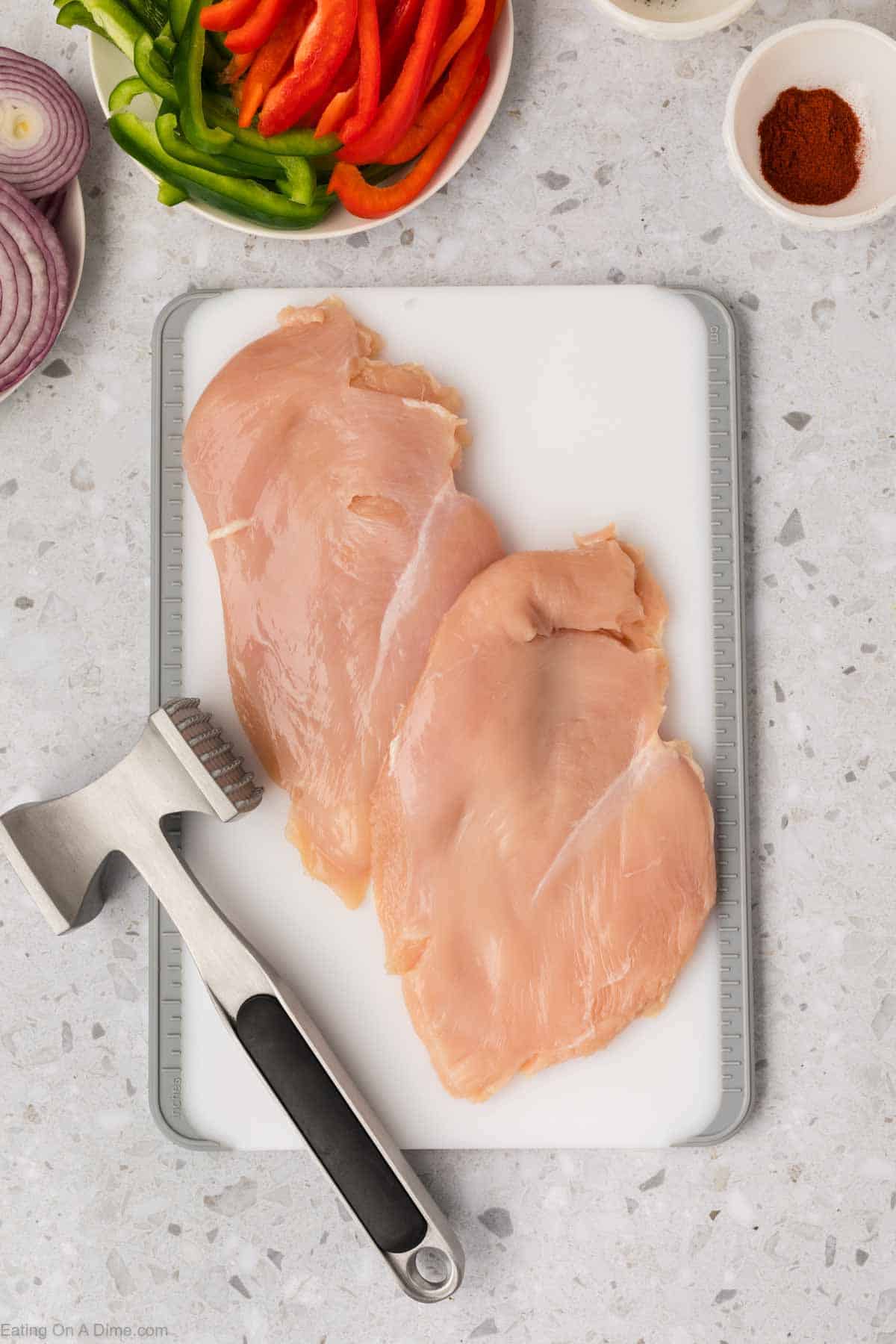 Pounded chicken on a cutting board with a meat mallet
