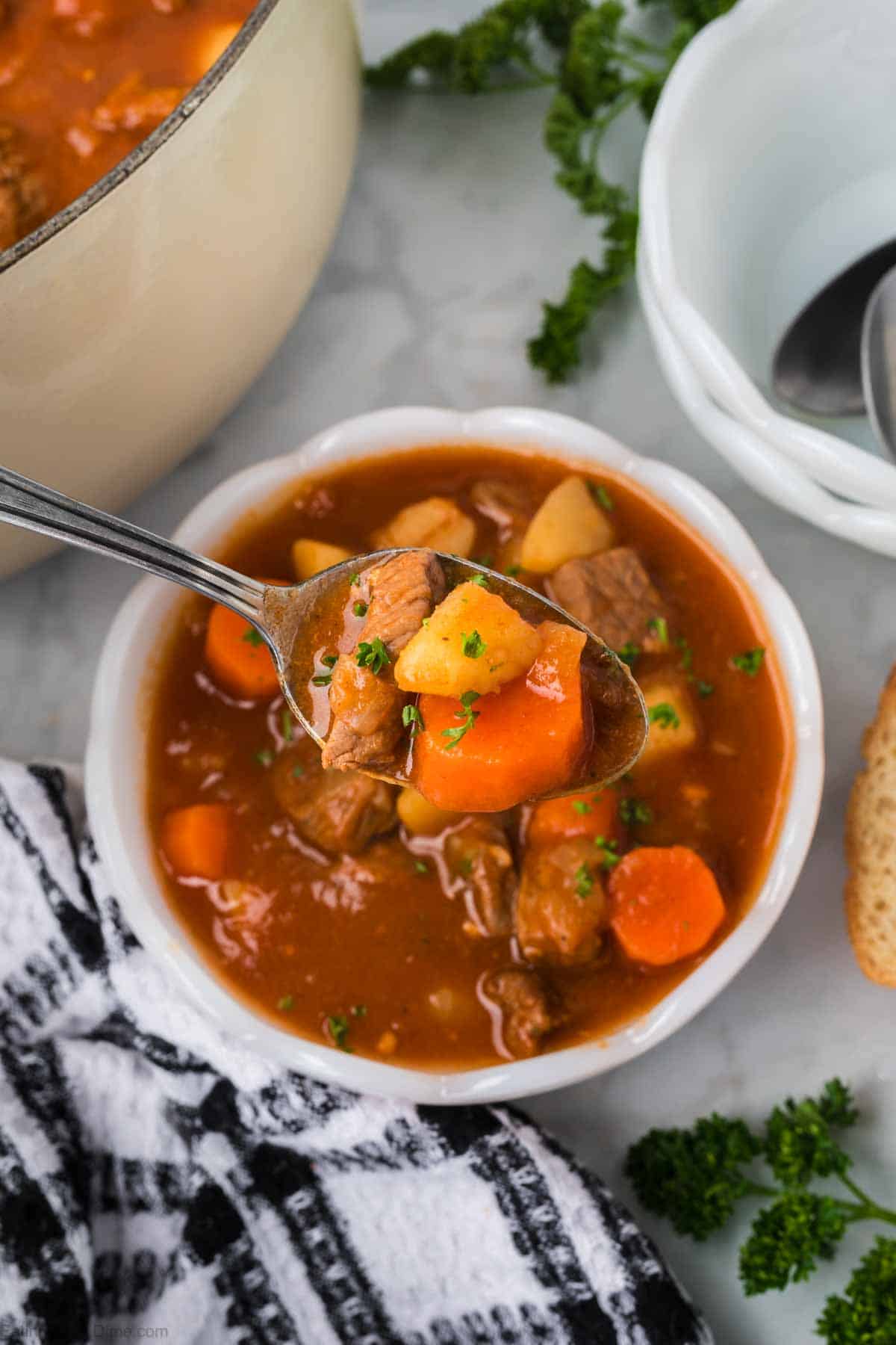 Hungary Goulash in a white bowl with a bite on spoon with diced carrots, meat and potatoes