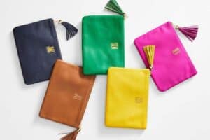 Five colorful leather pouches with tassel zip closures are arranged on a white surface. Each pouch, whether in navy blue, green, pink, brown, or yellow, is monogrammed with three gold letters—a perfect choice for Mother's Day gifts.