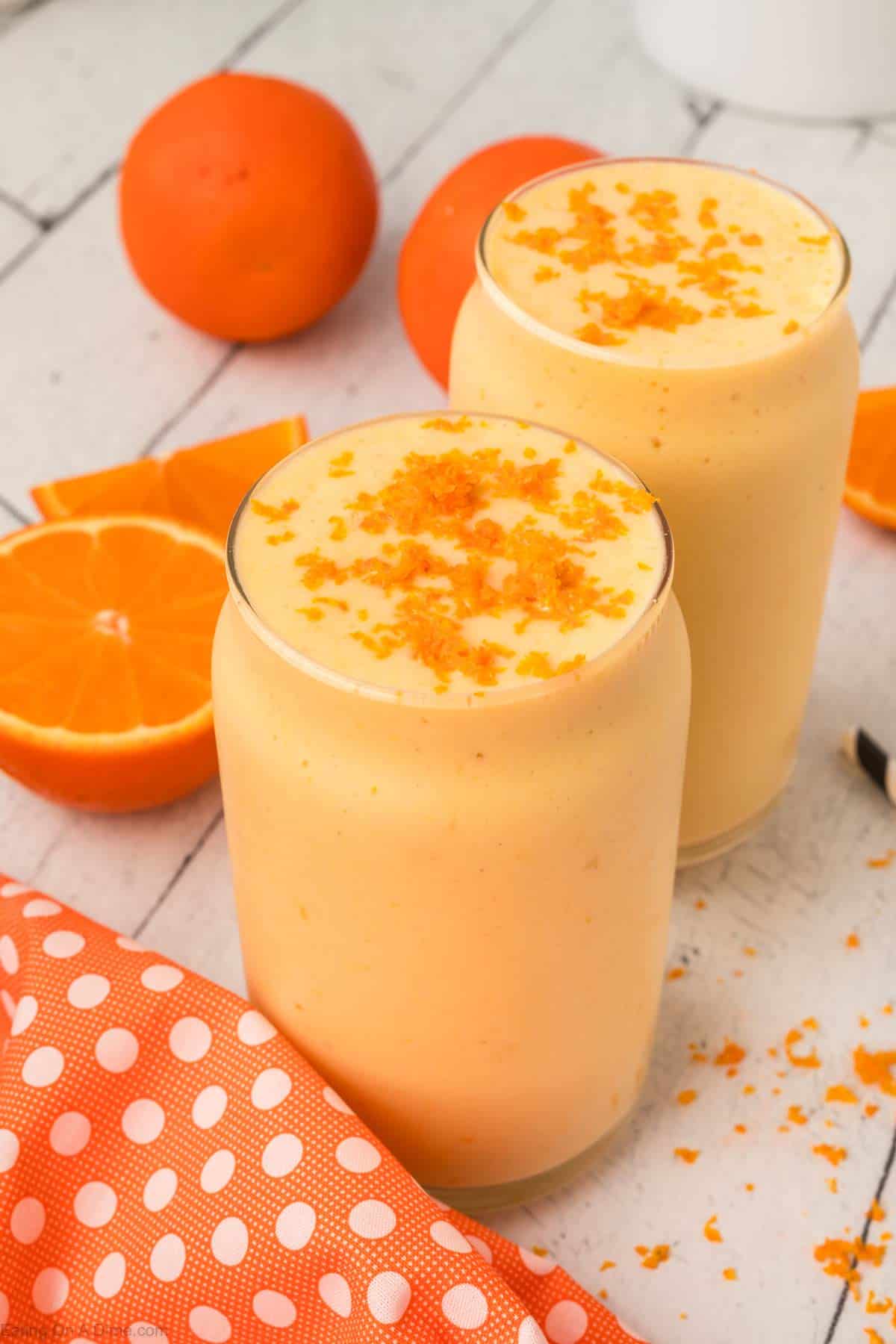 Orange Creamsicle Smoothies in a clear glasses topped with orange zest and fresh oranges on the side