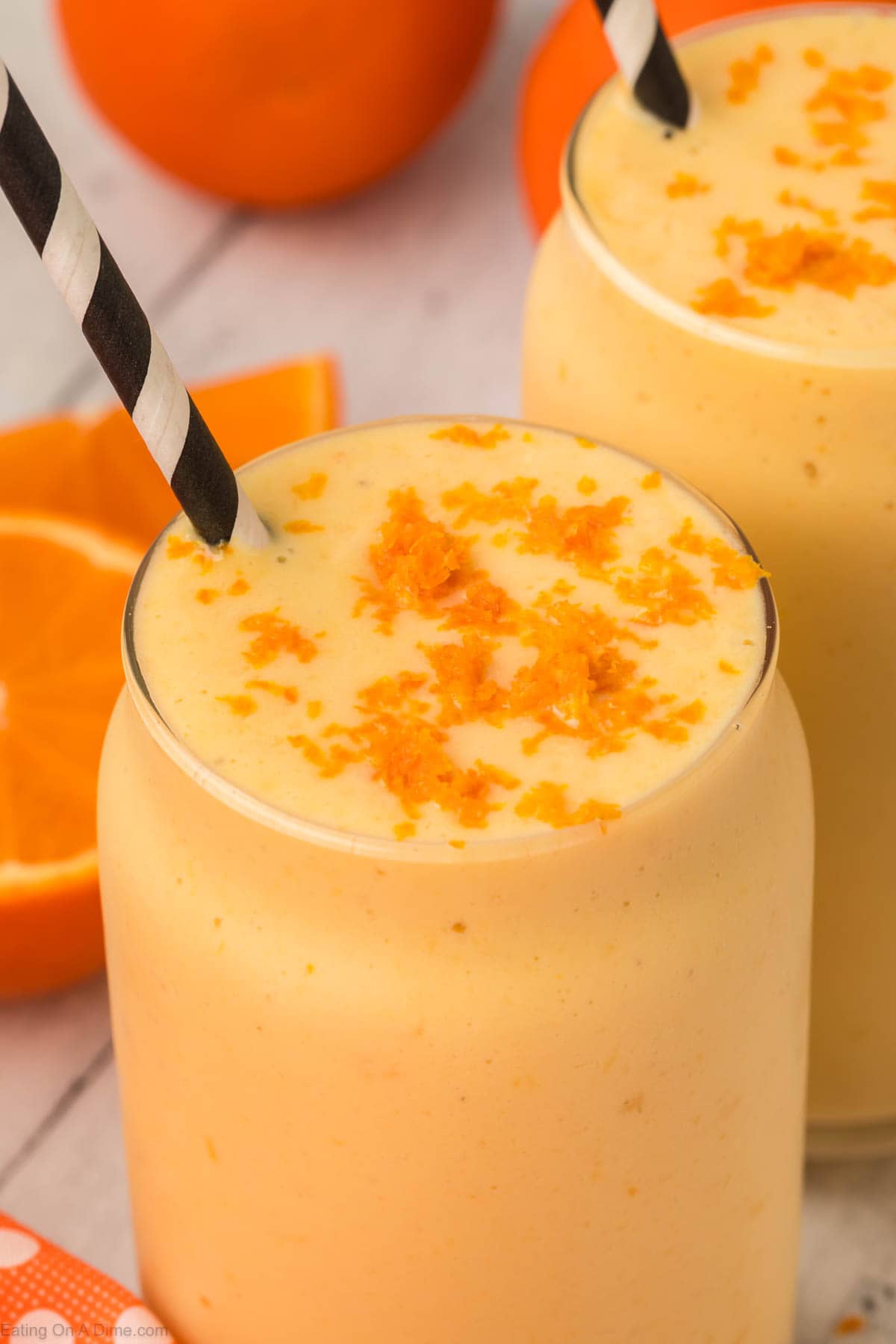 Orange Smoothie in a clear glass topped with orange zest with a straw