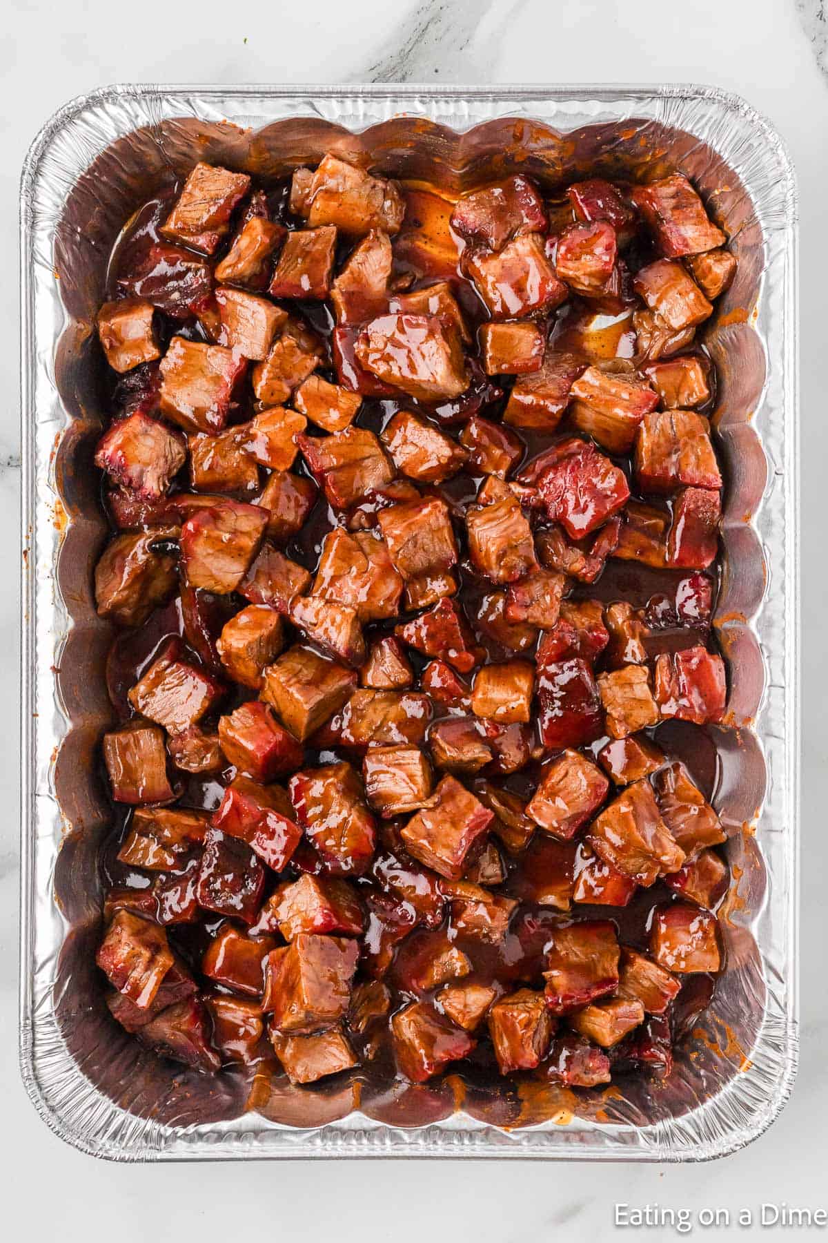 Diced meat in a foil pan drizzled with BBQ Sauce