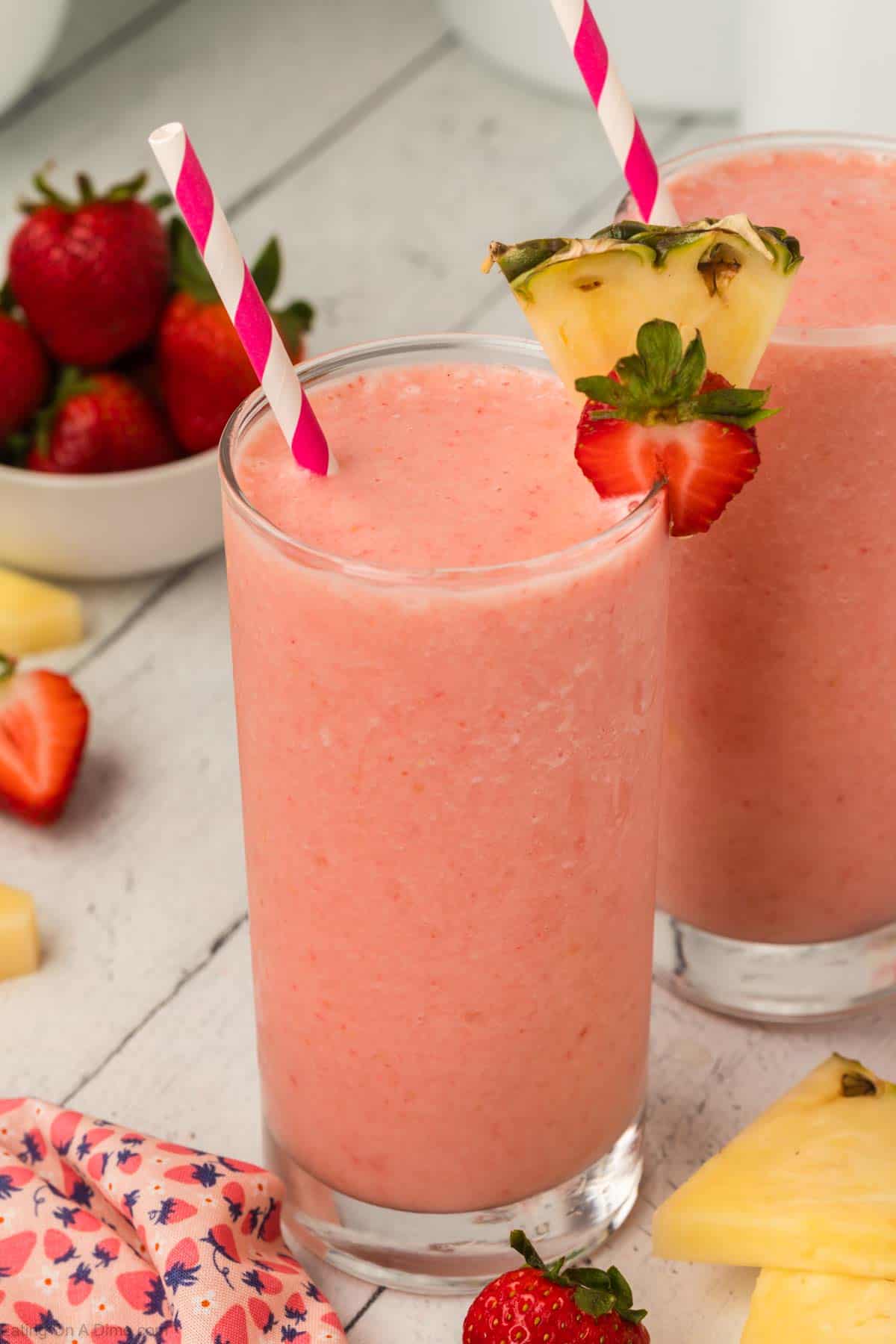 Strawberry pineapple smoothie in glasses topped with slice strawberries and fresh pineapple