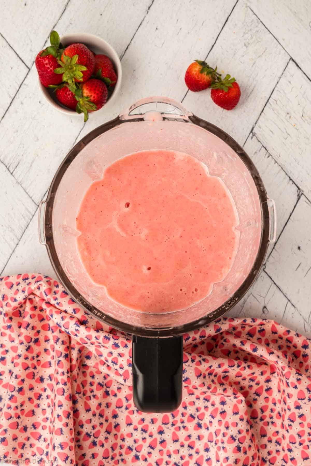 Smoothie blended in the blender with a bowl of fresh strawberries on the side