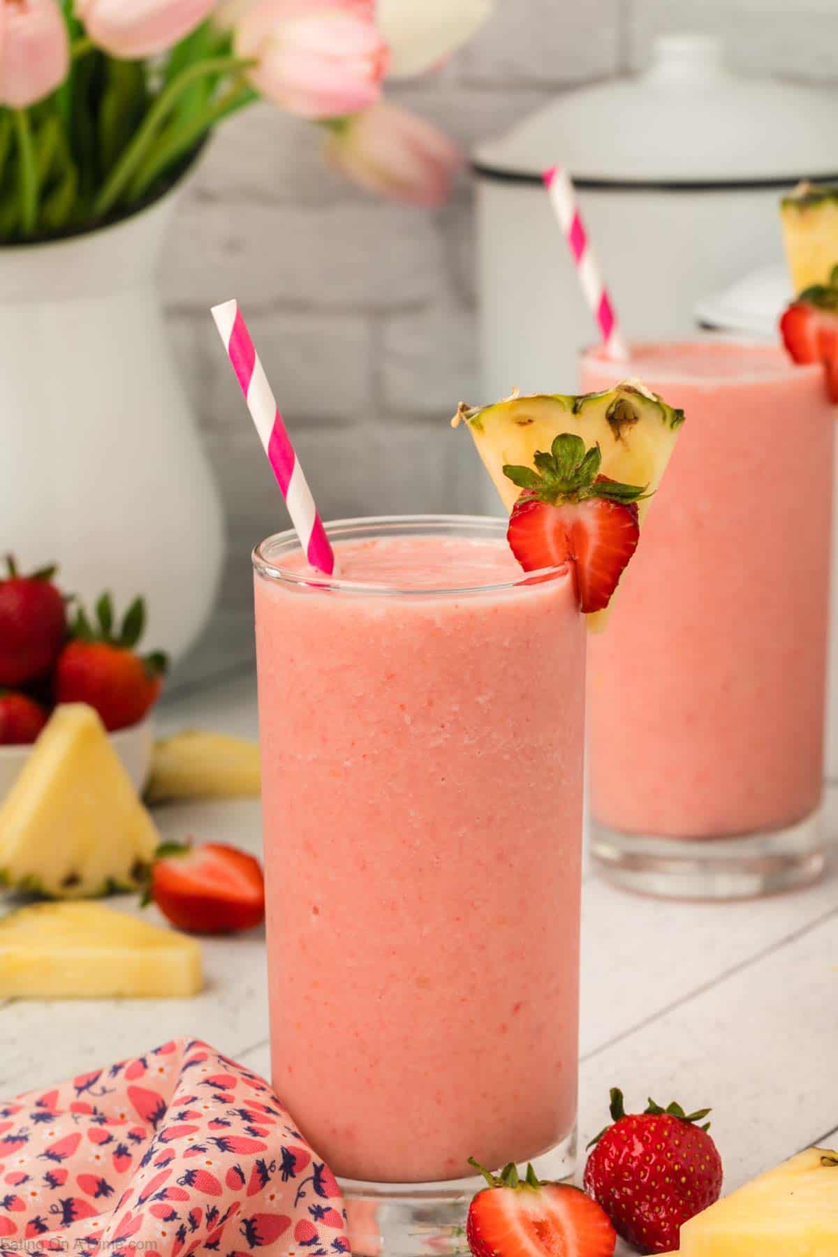 Strawberry pineapple smoothie in glasses topped with slice strawberries and fresh pineapple