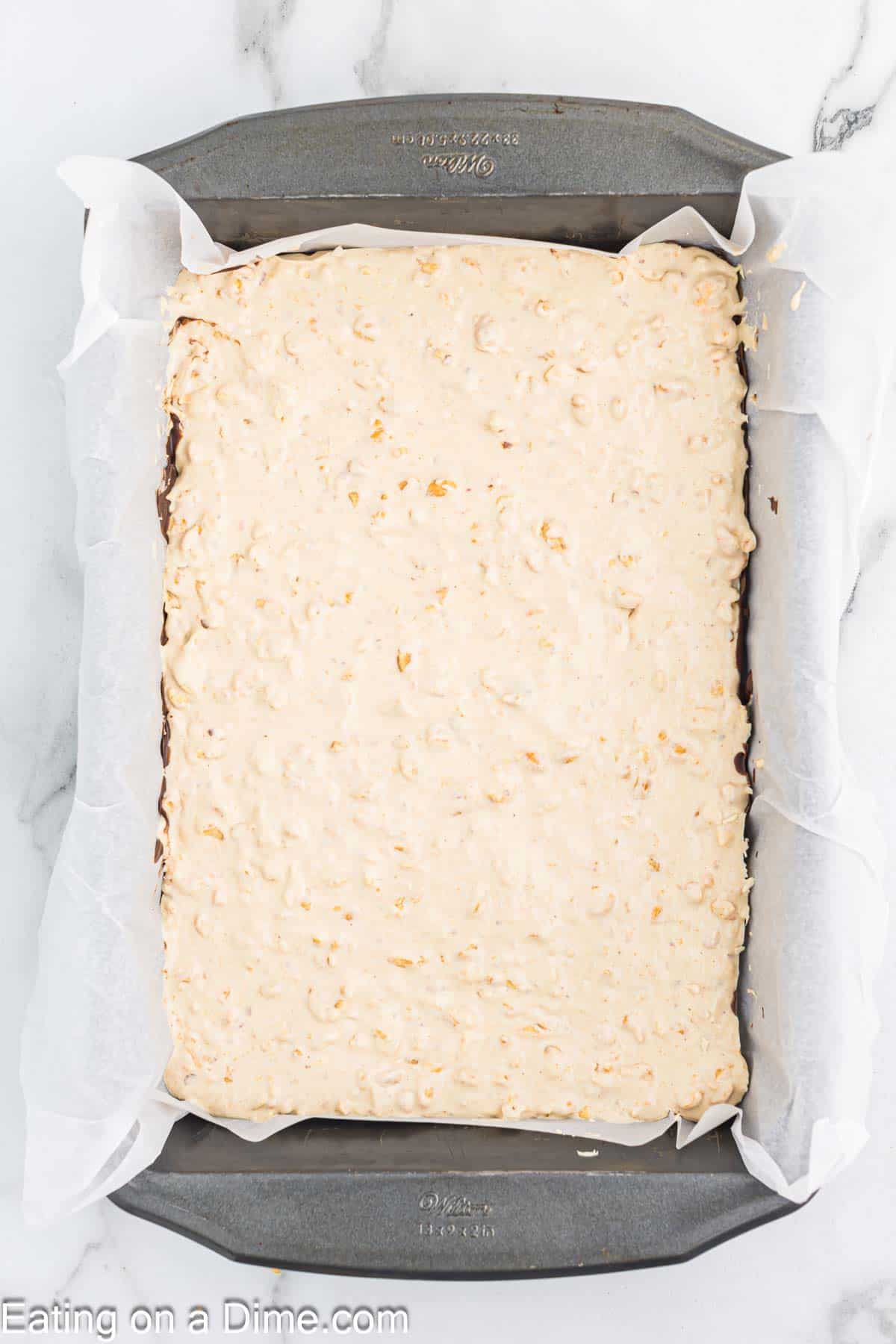 Spreading the nougat mixture over the chocolate mixture in the parchment paper lined baking dish