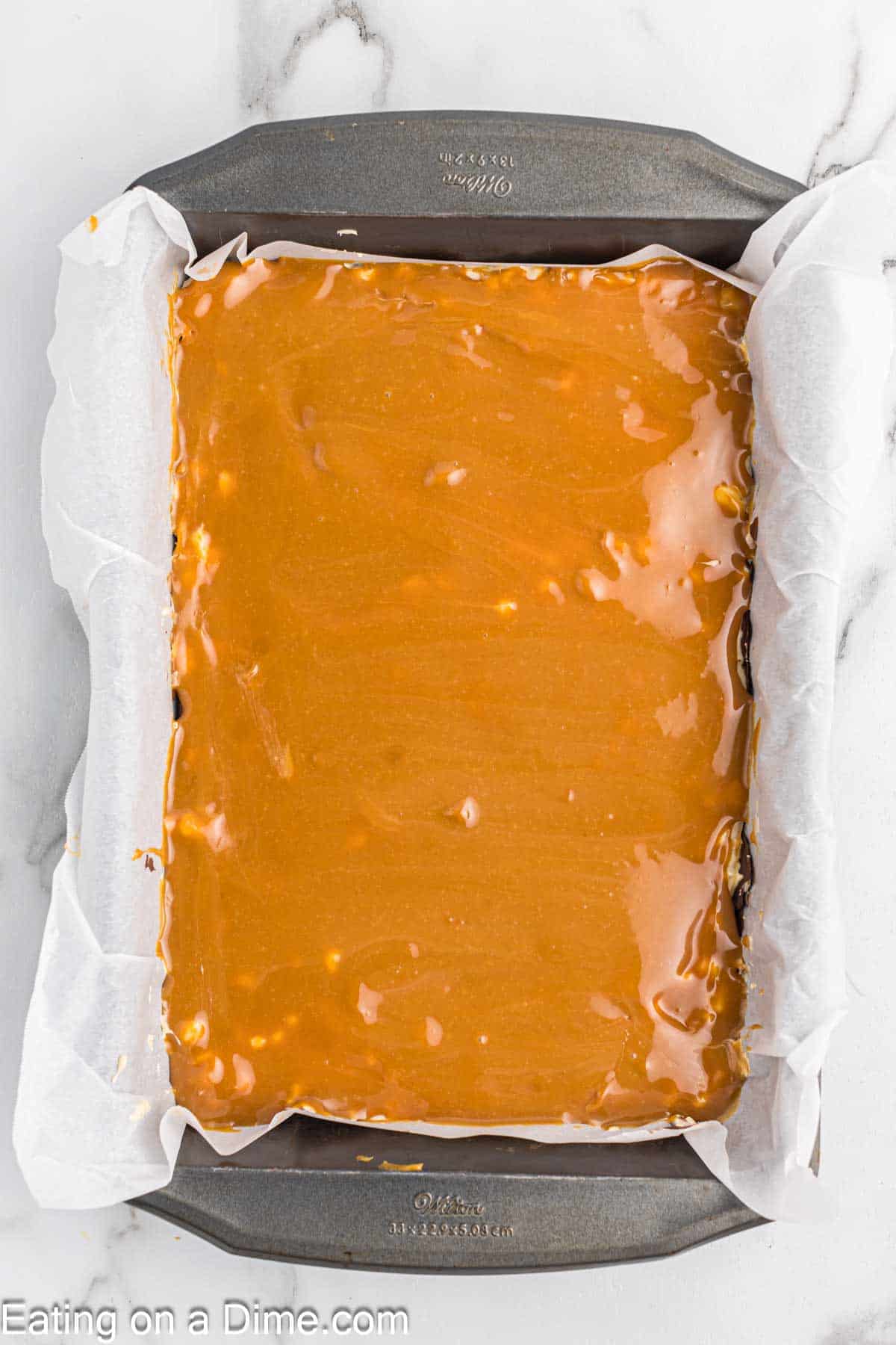 Pouring the caramel mixture over the nougat layer in the baking dish